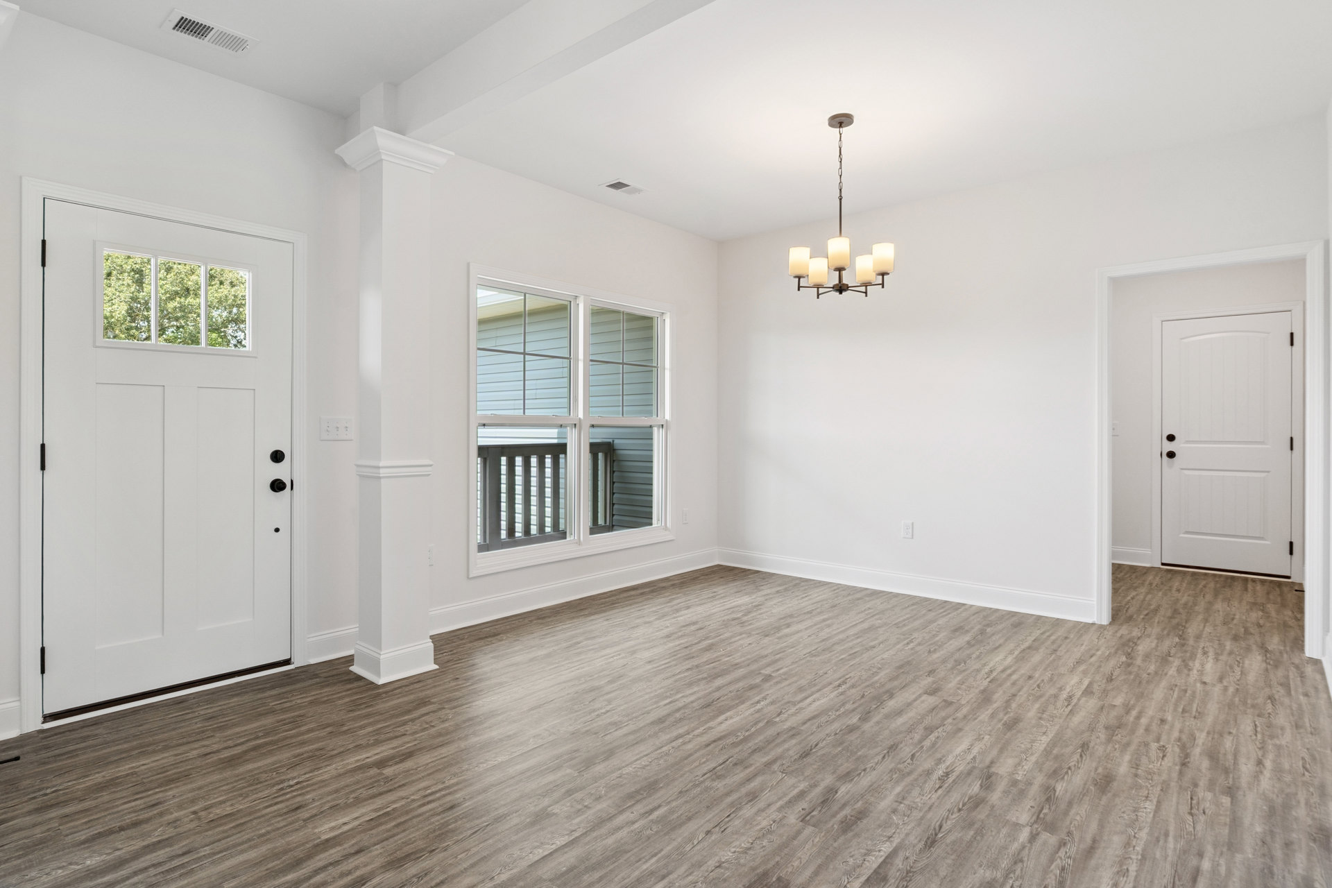Room with hardwood flooring, white double doors, large window with railing, plaster walls, and a chandelier suspended by a chain