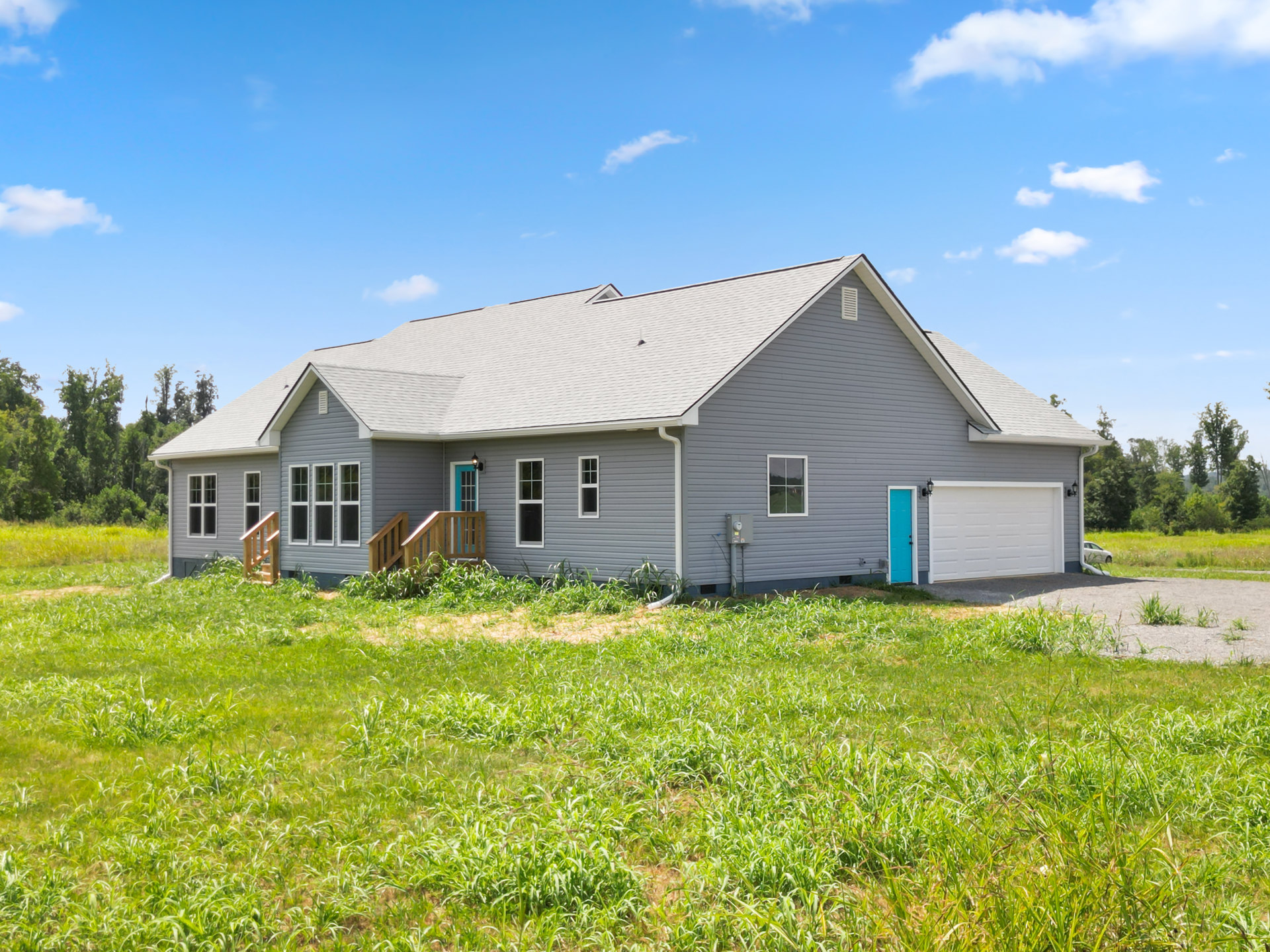 Two-story home with white siding, black roof, blue front door, attached white garage, second-floor balcony, grassy lawn, and wooden fence.