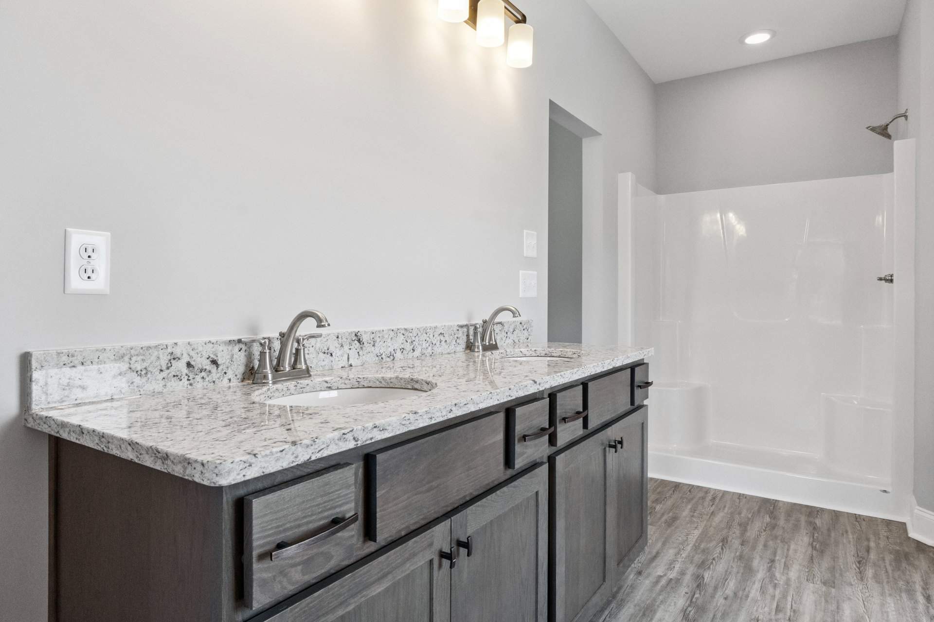 Bathroom featuring marble countertop with undermount sink, white cabinetry, chrome faucet, tiled shower enclosure, and modern light fixture