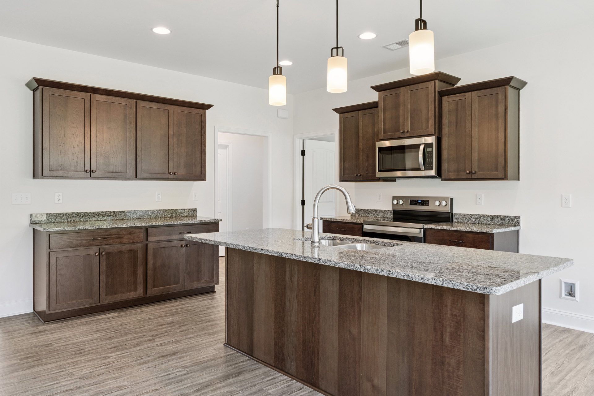 Marble countertop kitchen with undermount sink, open microwave, white cabinetry, granite surfaces, close-up of modern light fixture, and built-in appliances