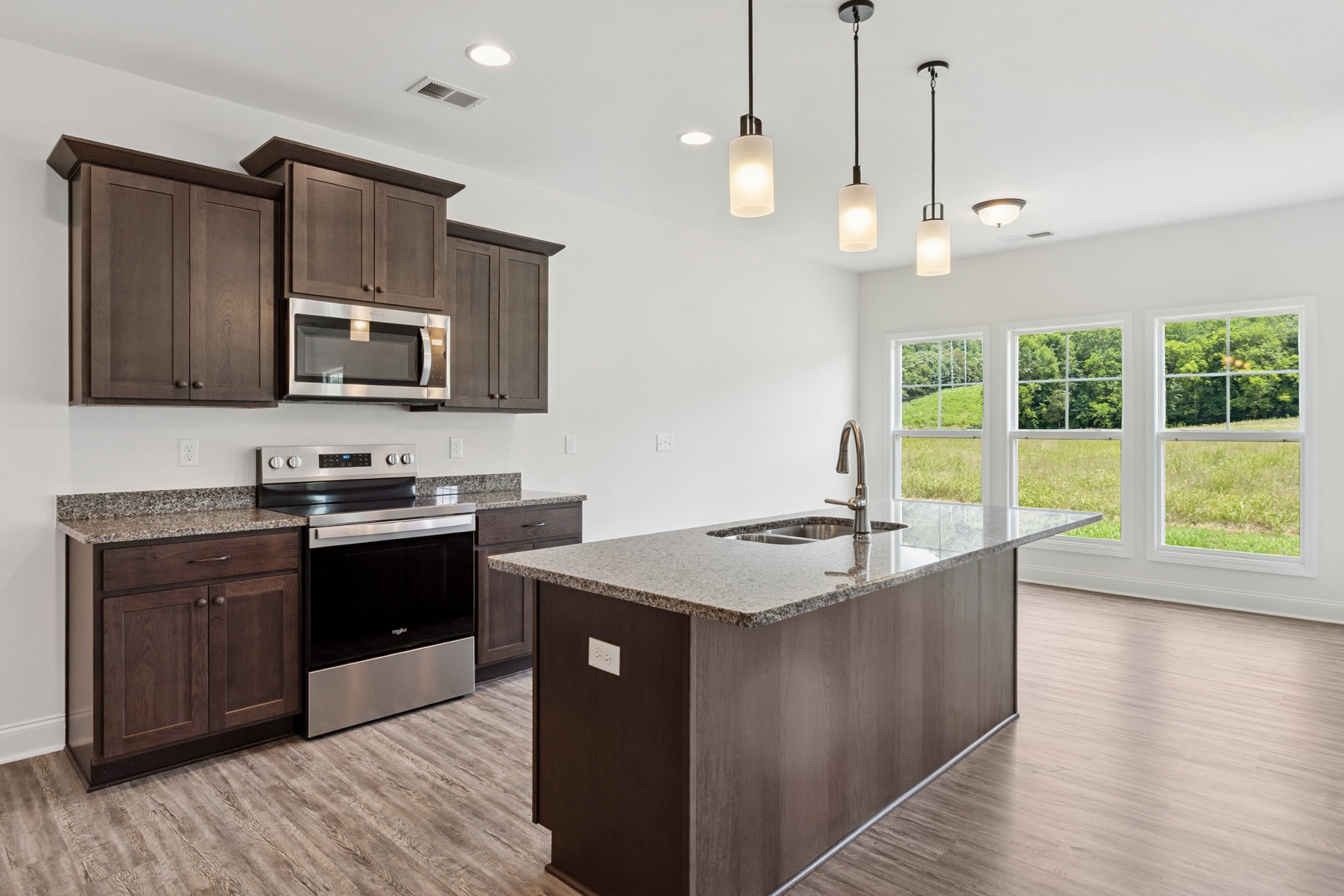 Spacious kitchen featuring a large central island with built-in sink, white countertops, stainless steel stove, microwave, light wood cabinetry, and wall outlets.