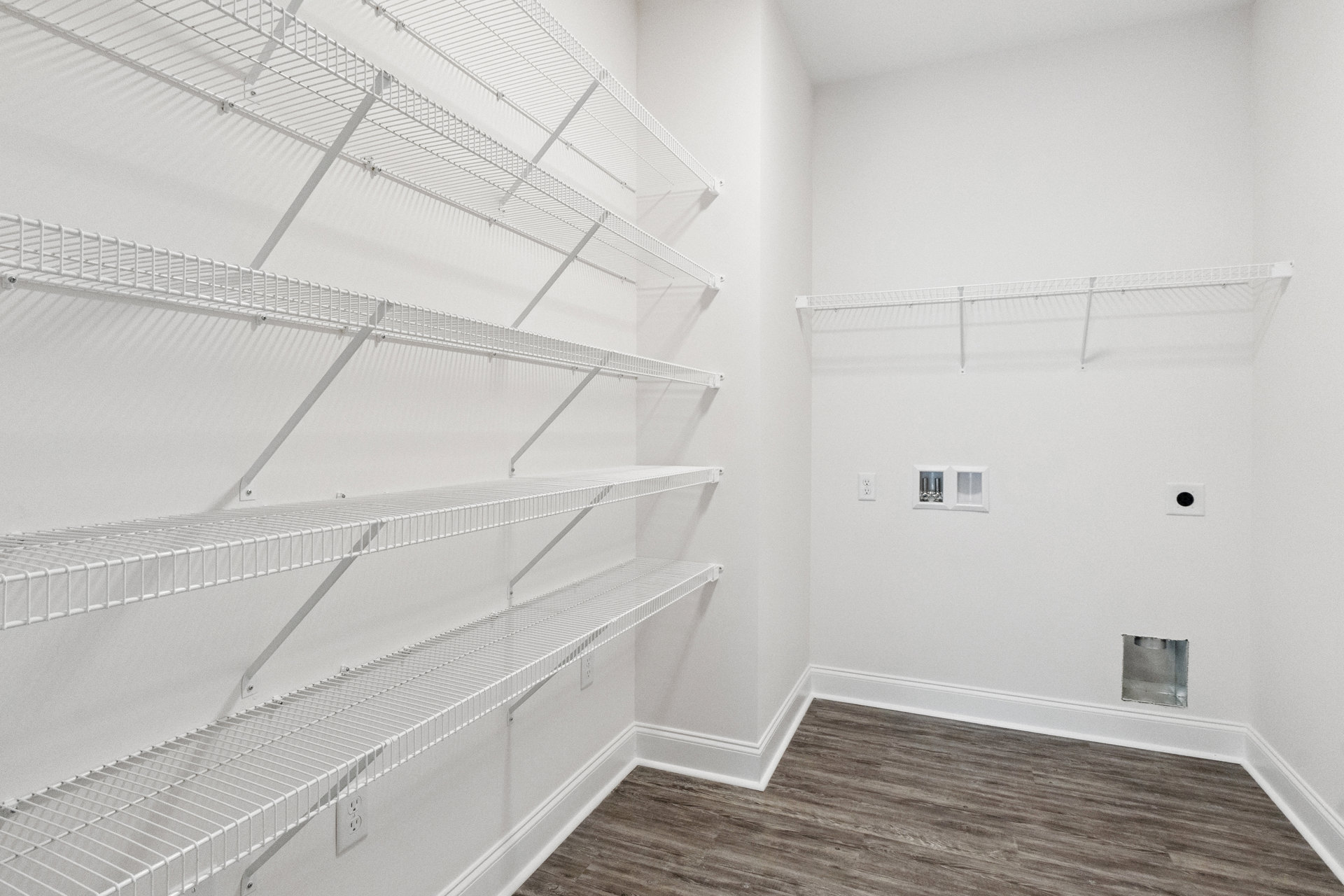 Built-in white shelving along a plaster wall, light wood flooring with white baseboard trim, recessed ceiling lighting, and a black circular outlet on a white surface