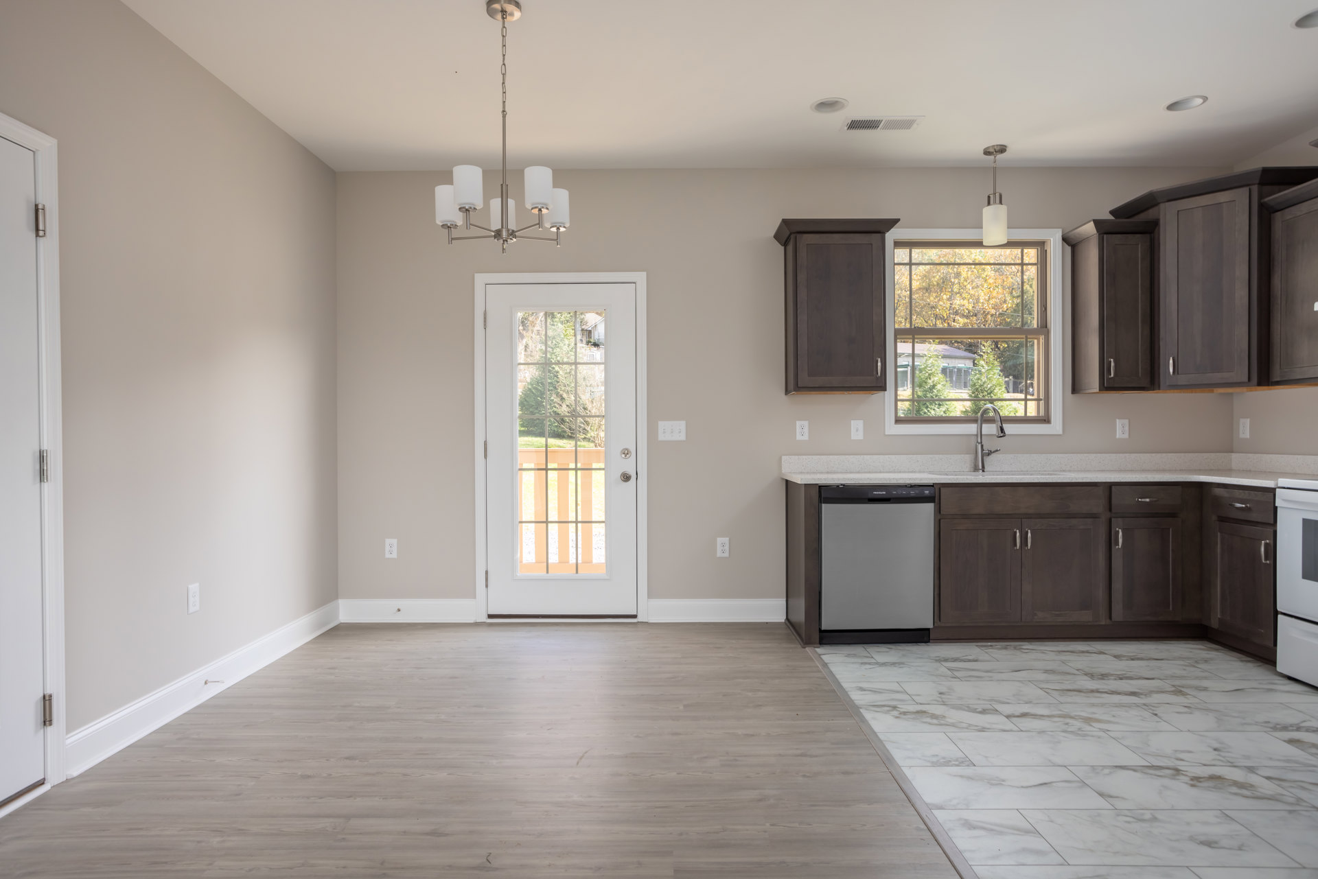 Open kitchen and dining area featuring light wood cabinetry, stone countertops, hardwood flooring, a glass-paneled door leading to a balcony, large window with tree views, and