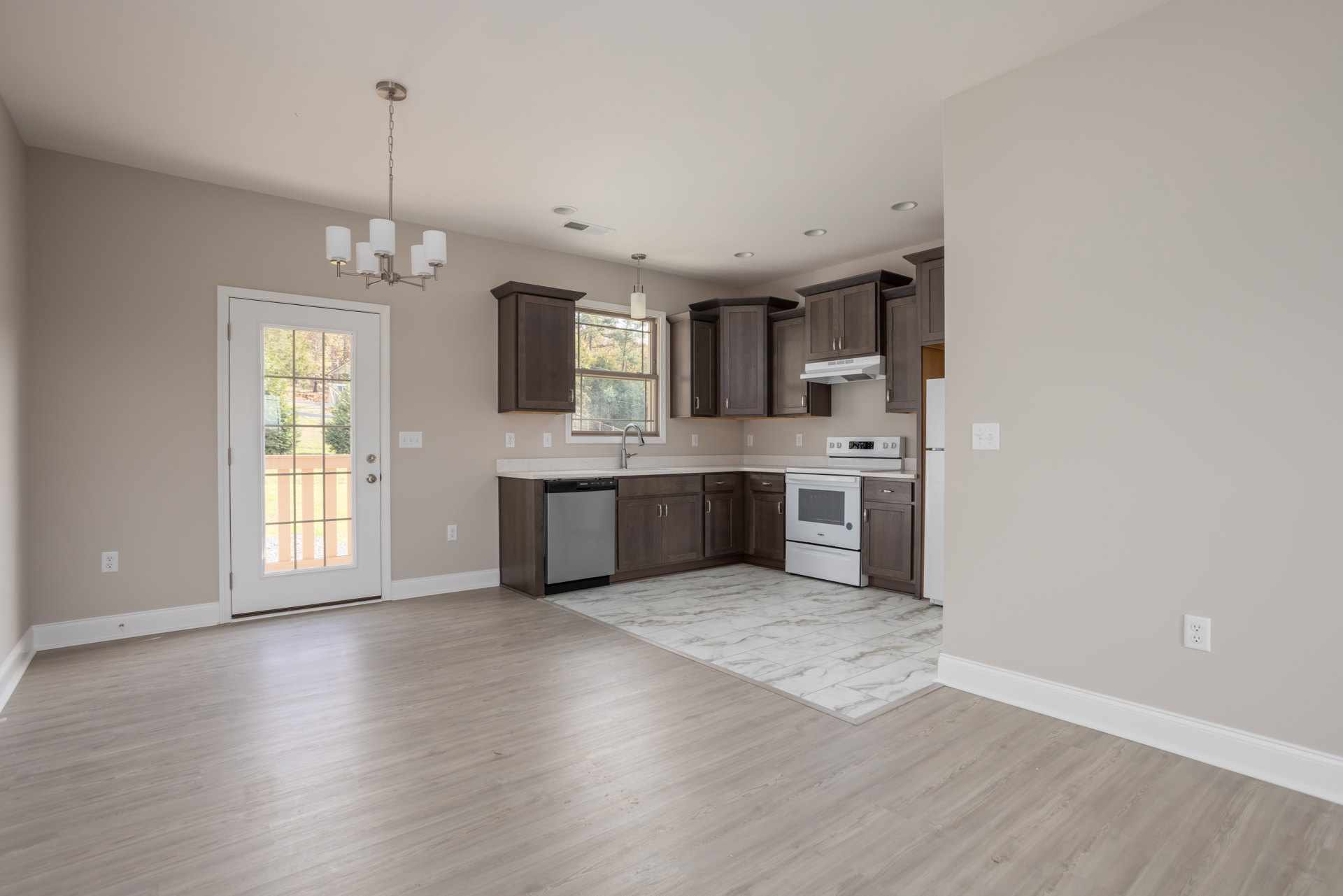 Open kitchen and dining area with hardwood floors, white cabinetry, white stove and oven, door with window, and rectangular kitchen island with black countertop.