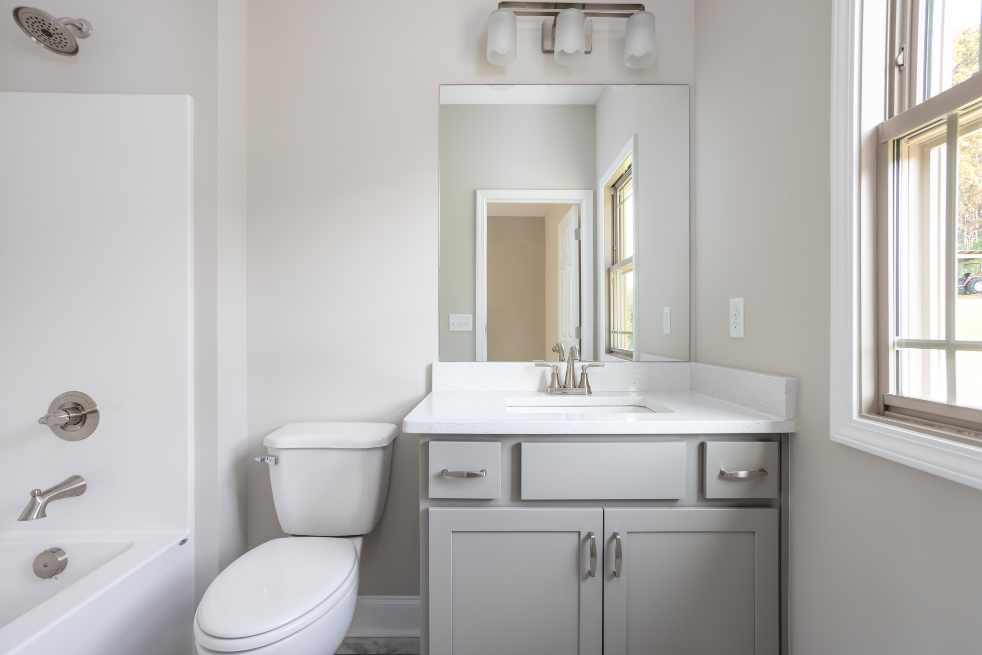 Modern bathroom with white porcelain toilet, rectangular sink on a floating vanity, silver faucet and toilet handle, light gray tile flooring, and white walls