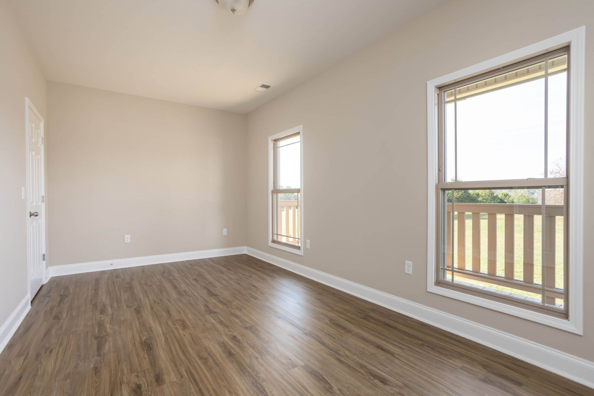Wood flooring in a bright room with large white-framed windows overlooking a grassy field and fence