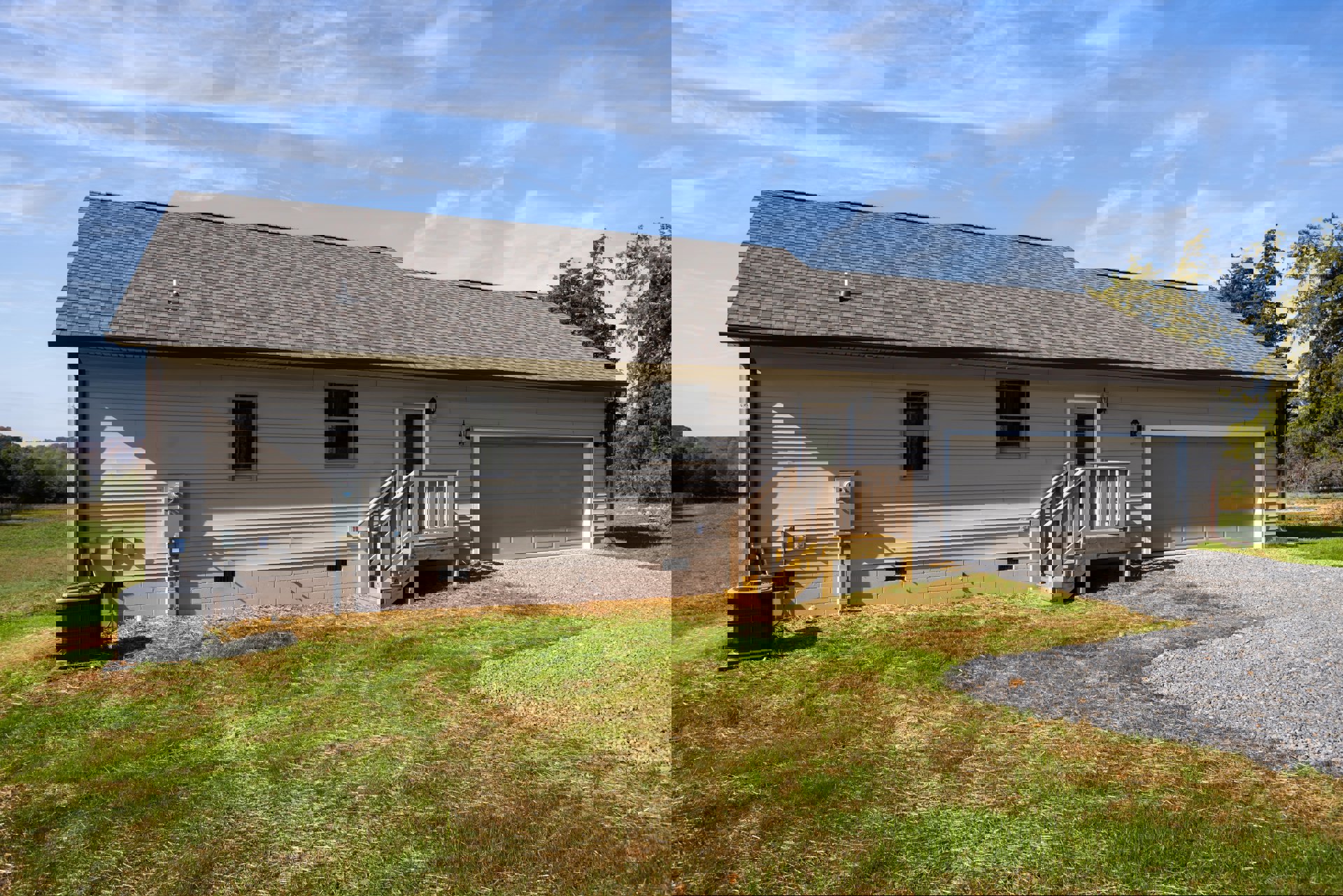 Two-story home with attached garage, wooden exterior staircase, white-framed windows, dark window trim, black and grey heat pump, and green grass lawn
