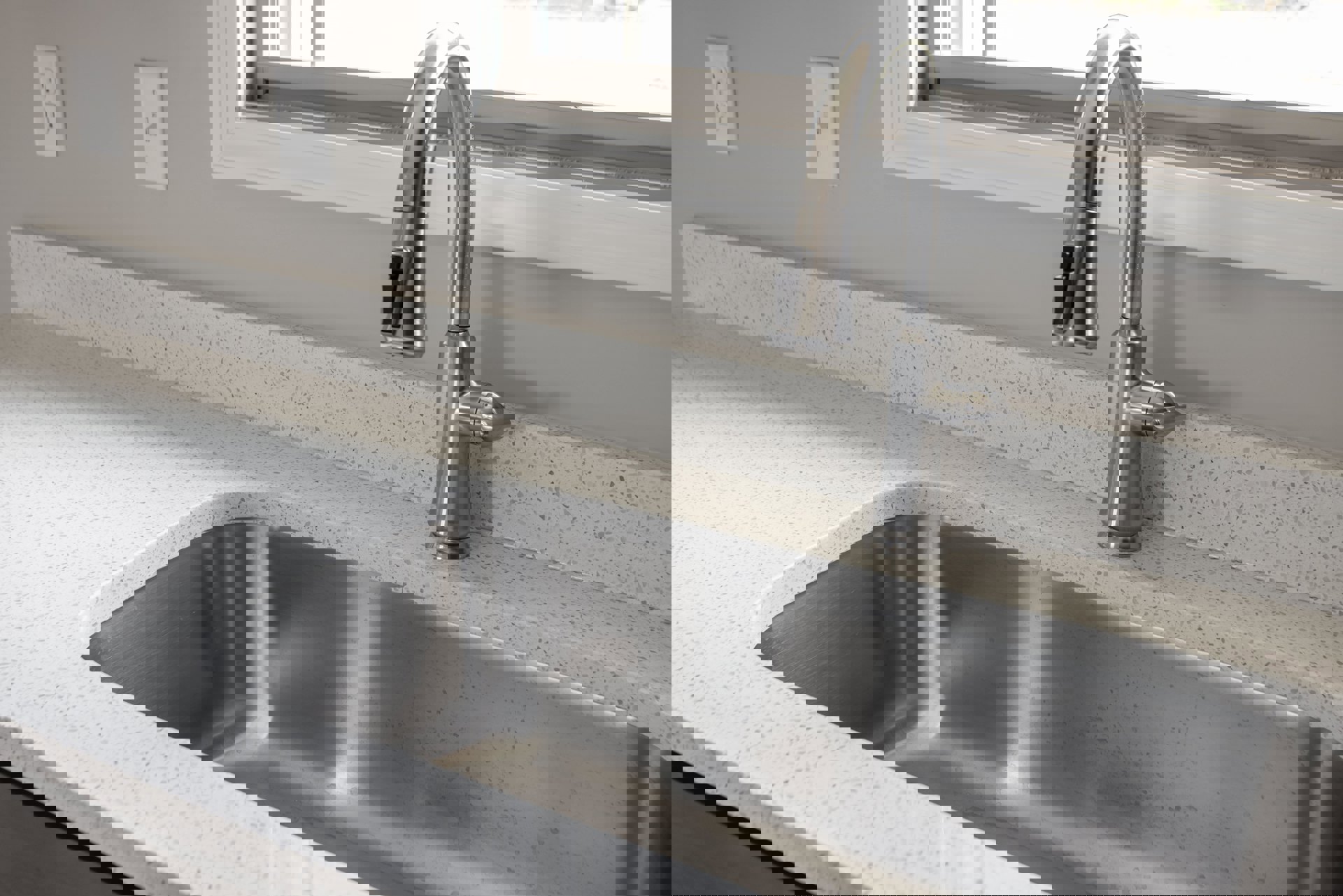 Stainless steel kitchen sink with modern silver faucet, black handle, white tile backsplash, electrical outlet, and light switch on wall