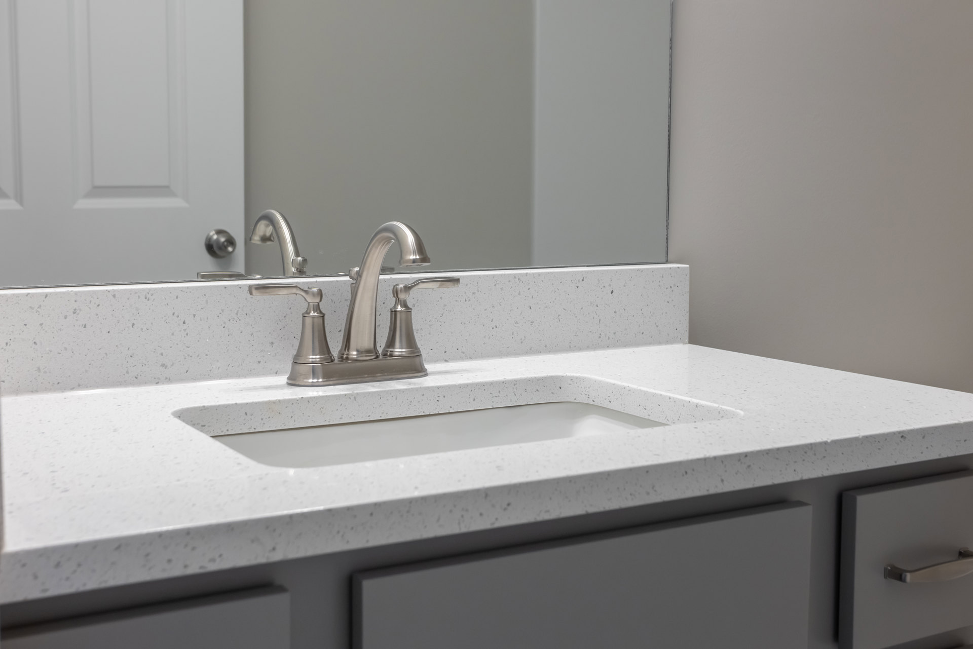 White quartz countertop with undermount sink, brushed silver faucet, frameless mirror, light gray tile backsplash, and flat-panel vanity drawer with silver knob