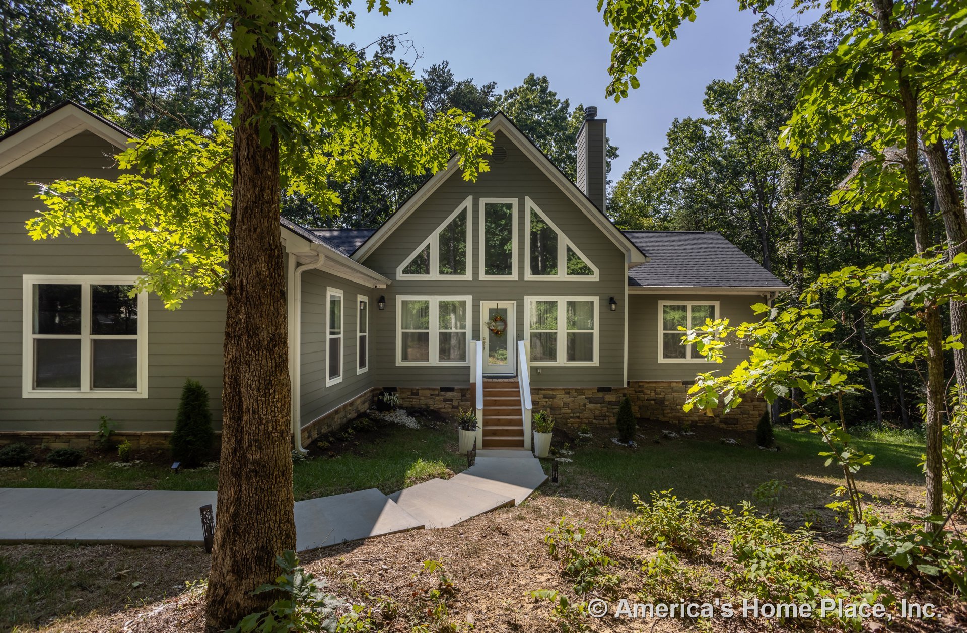 Two-story home with white-framed windows, covered porch, expansive green front yard, mature trees surrounding property, blue sky overhead