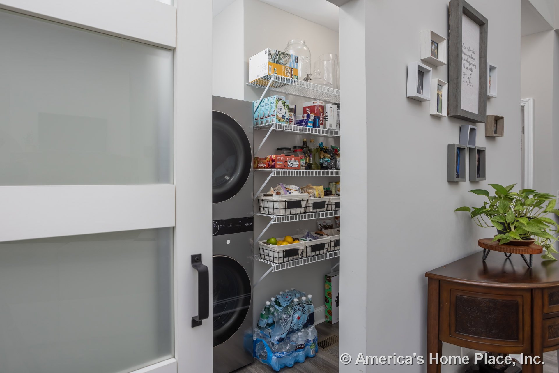 Laundry room featuring white cabinetry, open white door with stripe detail, potted plant on tabletop, large water bag, bowl on table, and circular decor object.