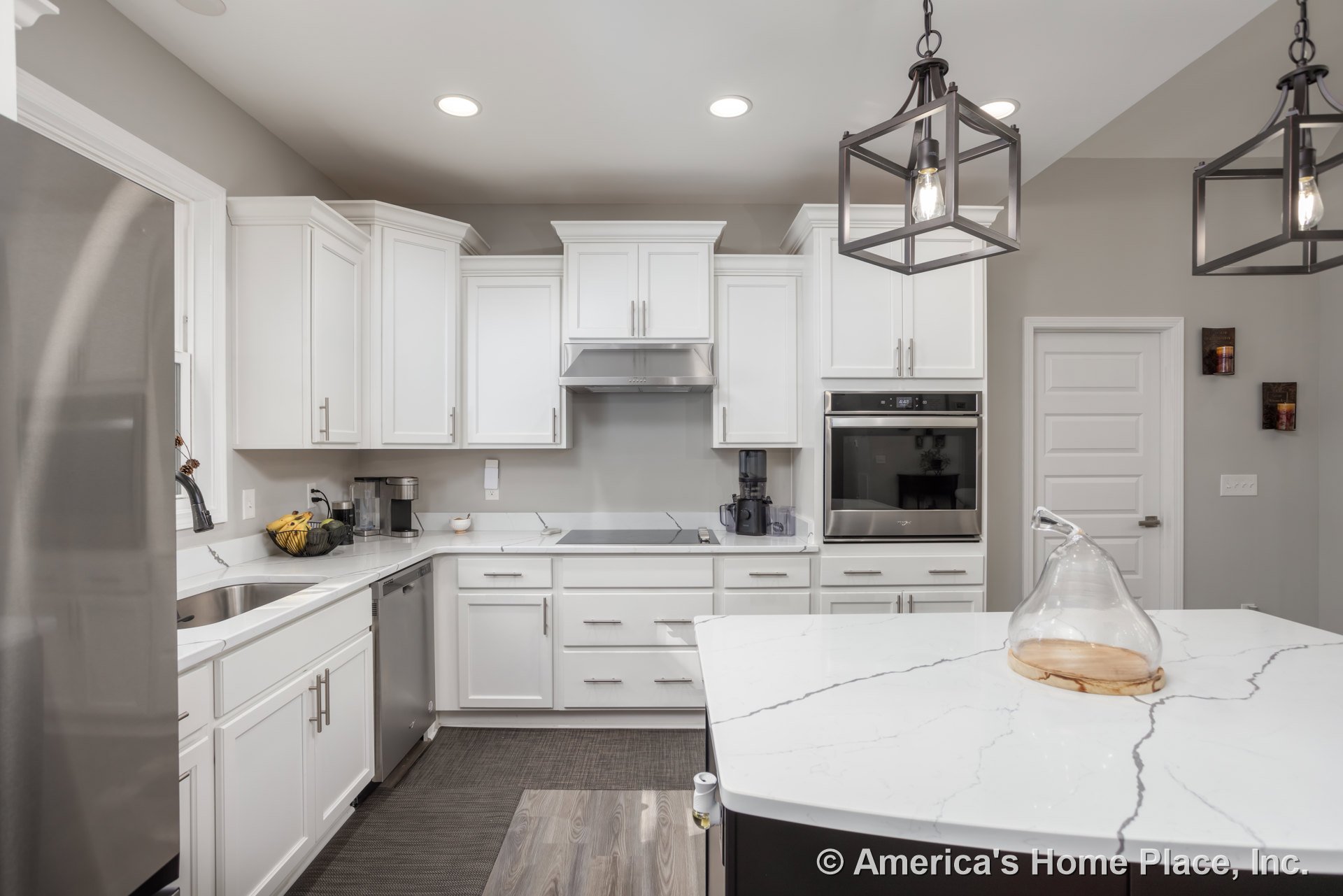 White shaker cabinets and black island with quartz countertop, stainless steel oven, silver refrigerator, glass containers on wood tray, bowl of bananas and avocados on counter