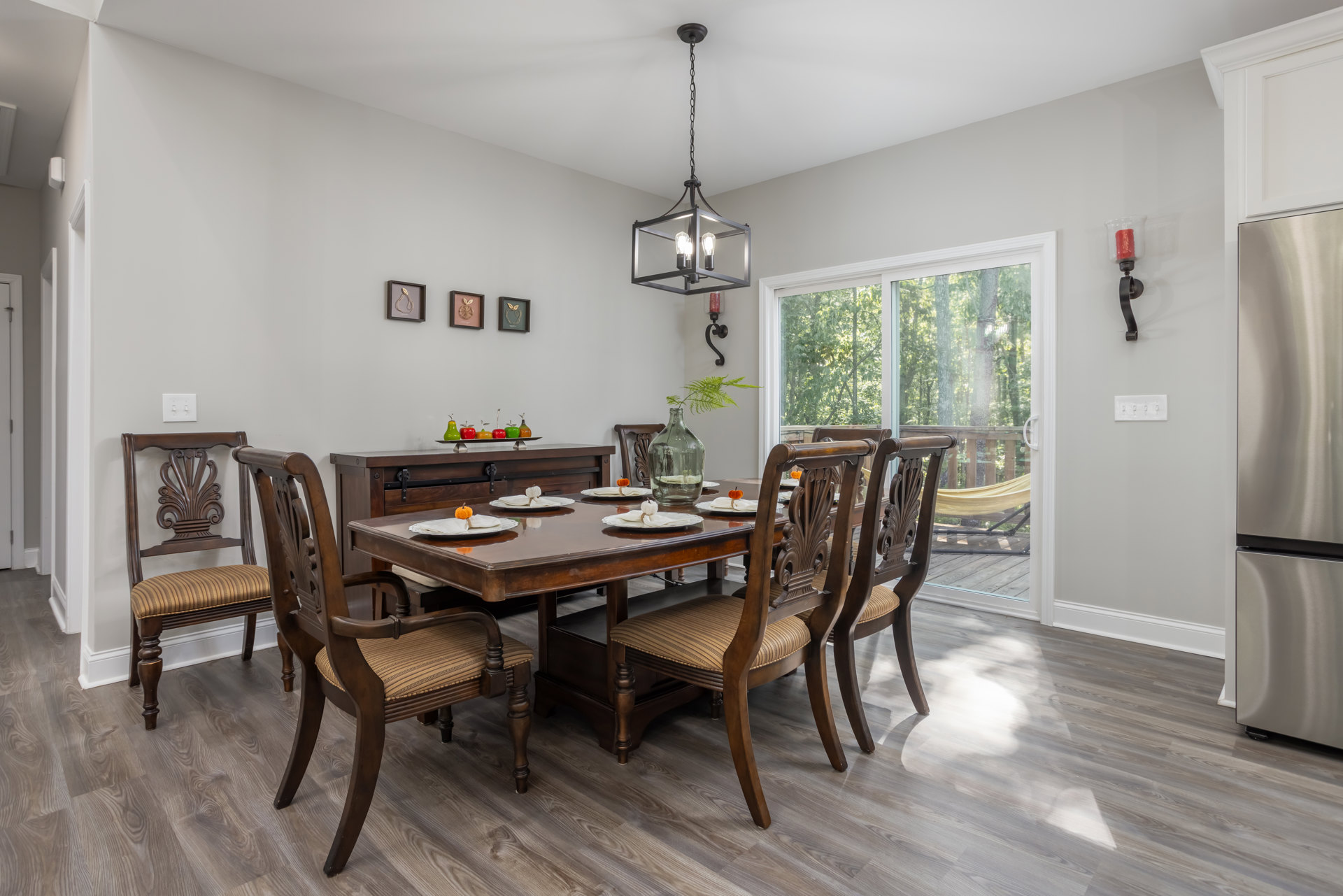 Wood dining table set with carved-back chairs, plates, and glass bottle centerpiece, laminate flooring, framed pear artwork on wall