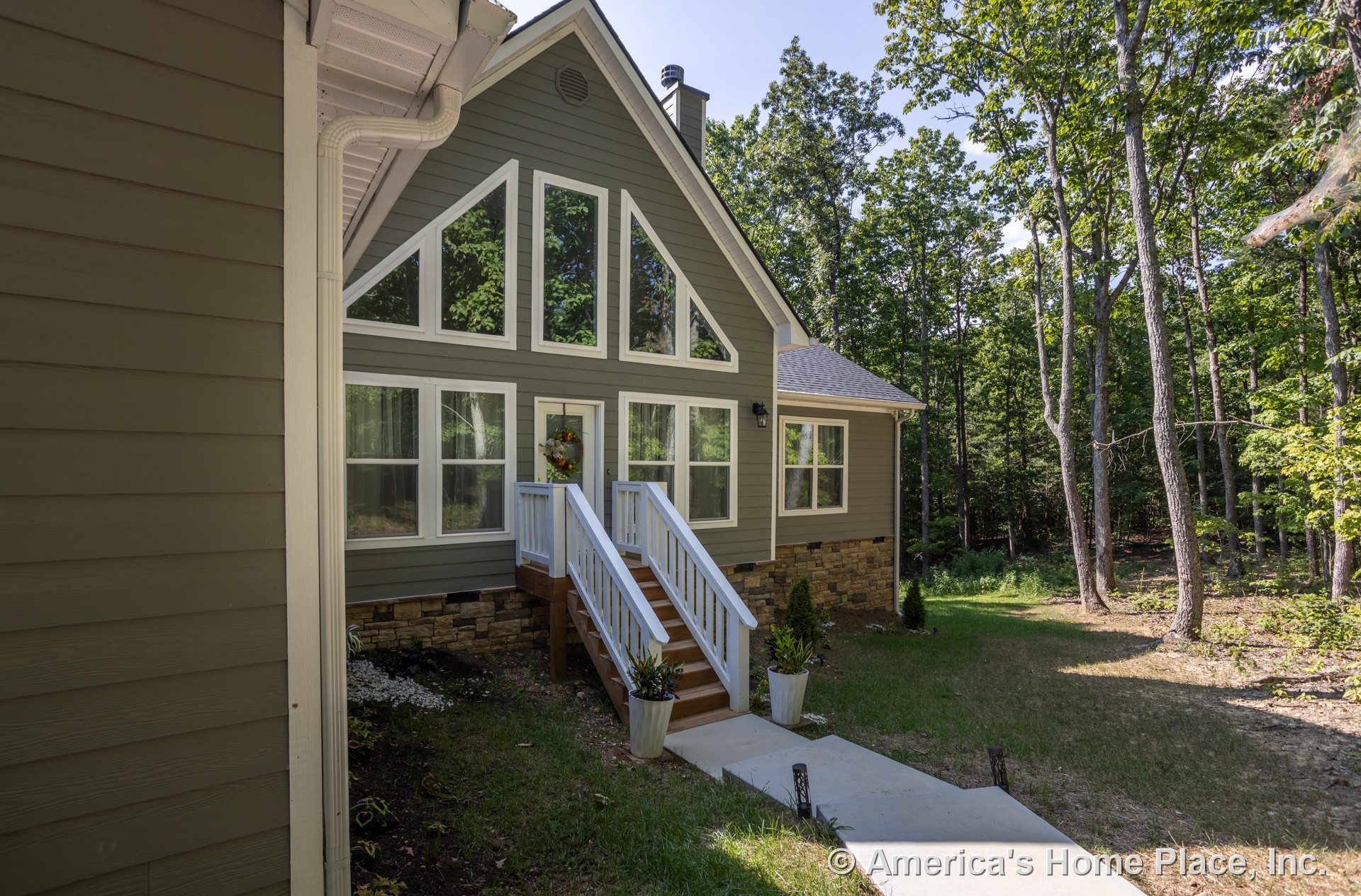 Two-story home with white siding, covered porch, wooden stairs with white railings, potted plants, large windows, and trees visible in the background