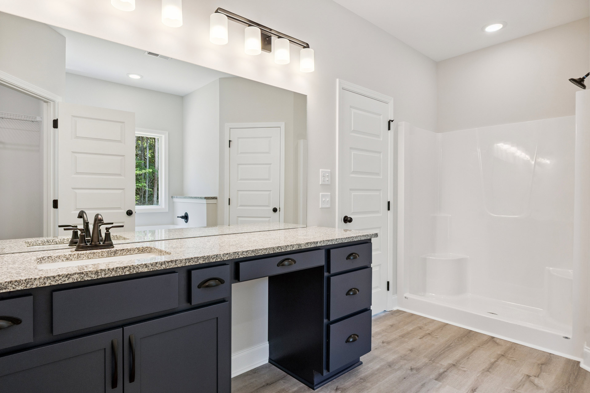 Modern bathroom featuring a white sink with chrome faucet, glass-enclosed shower with wood-look tile flooring, white door with black handle, recessed ceiling light, and window