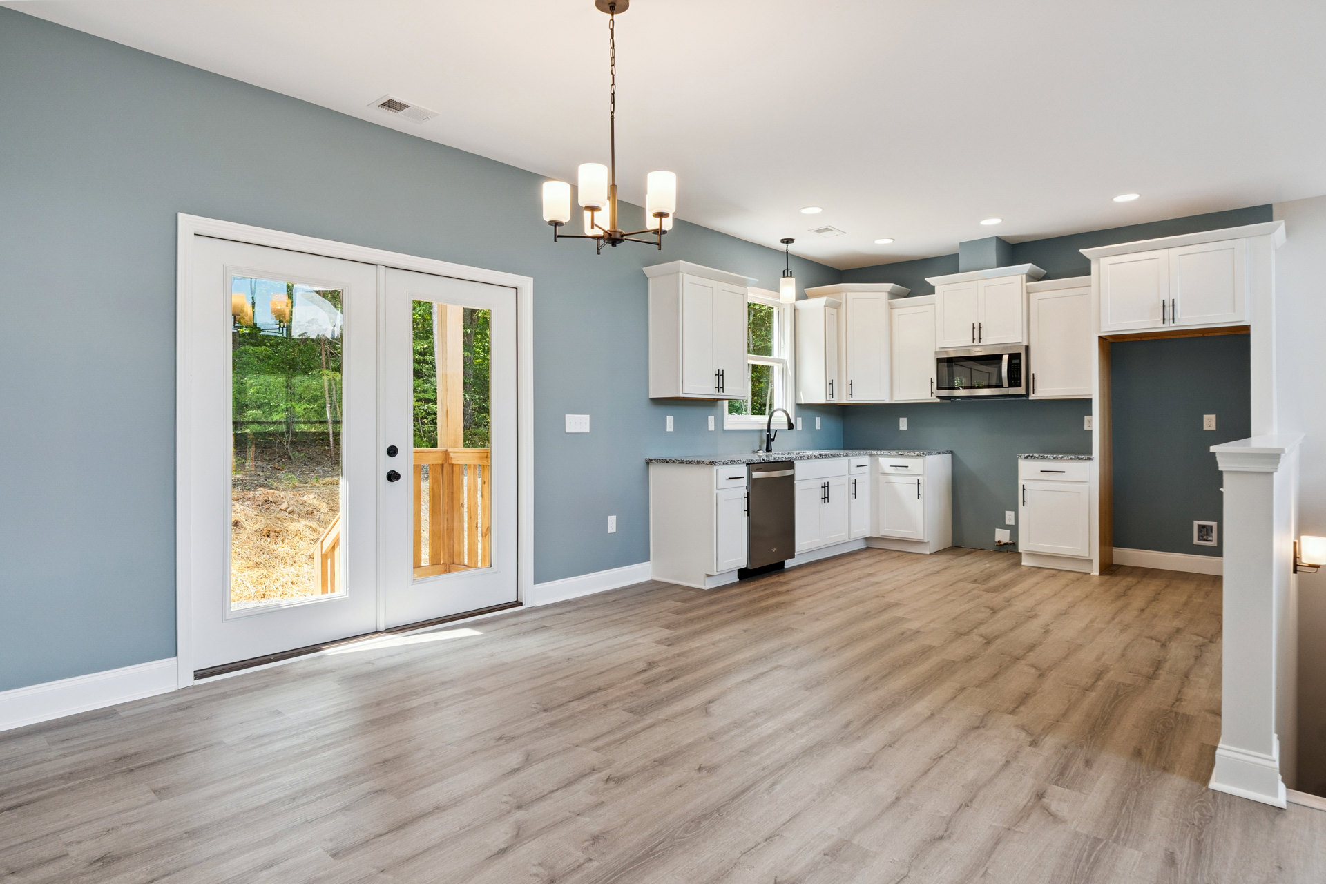 Open kitchen and dining area featuring white cabinetry, black hardware, hardwood flooring, white countertops, built-in microwave, and double glass-paneled doors.