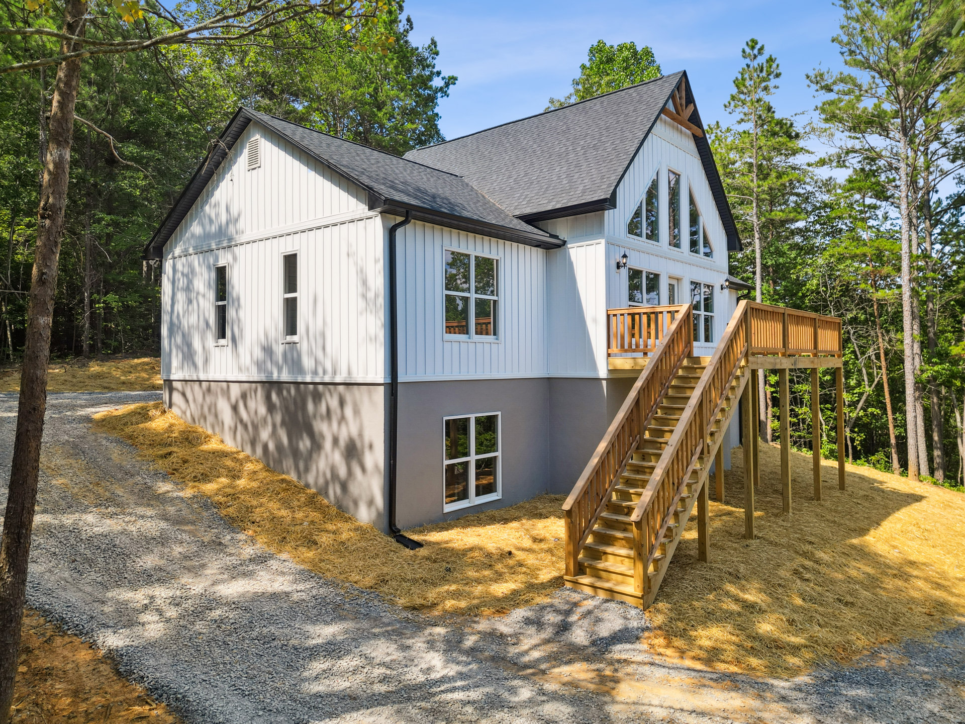Two-story home with exterior wood staircase, white-framed windows reflecting nearby trees, and wooden siding surrounded by greenery.