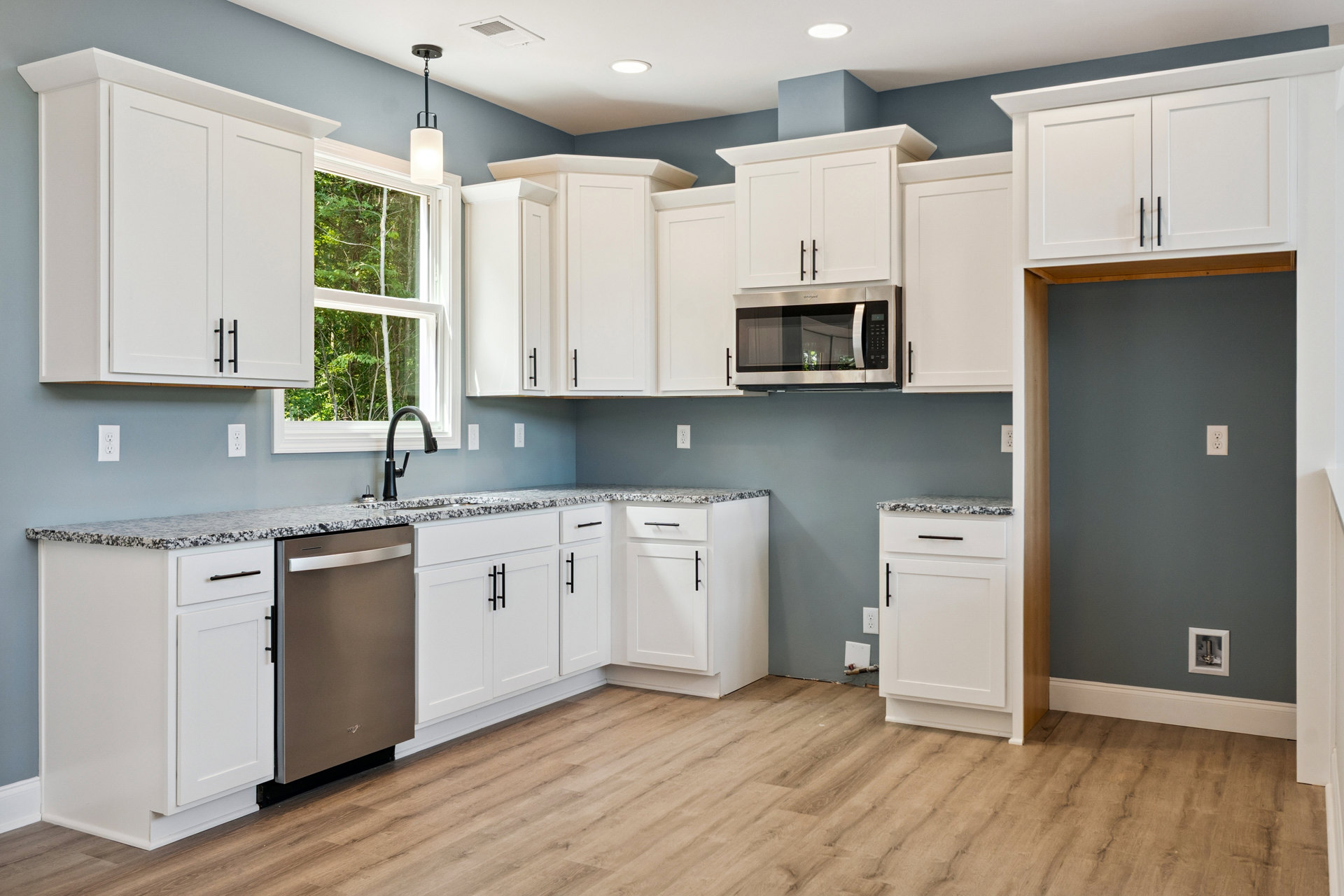 White kitchen cabinets with black handles, stainless steel dishwasher and refrigerator, built-in microwave, light fixture, and neutral countertops.