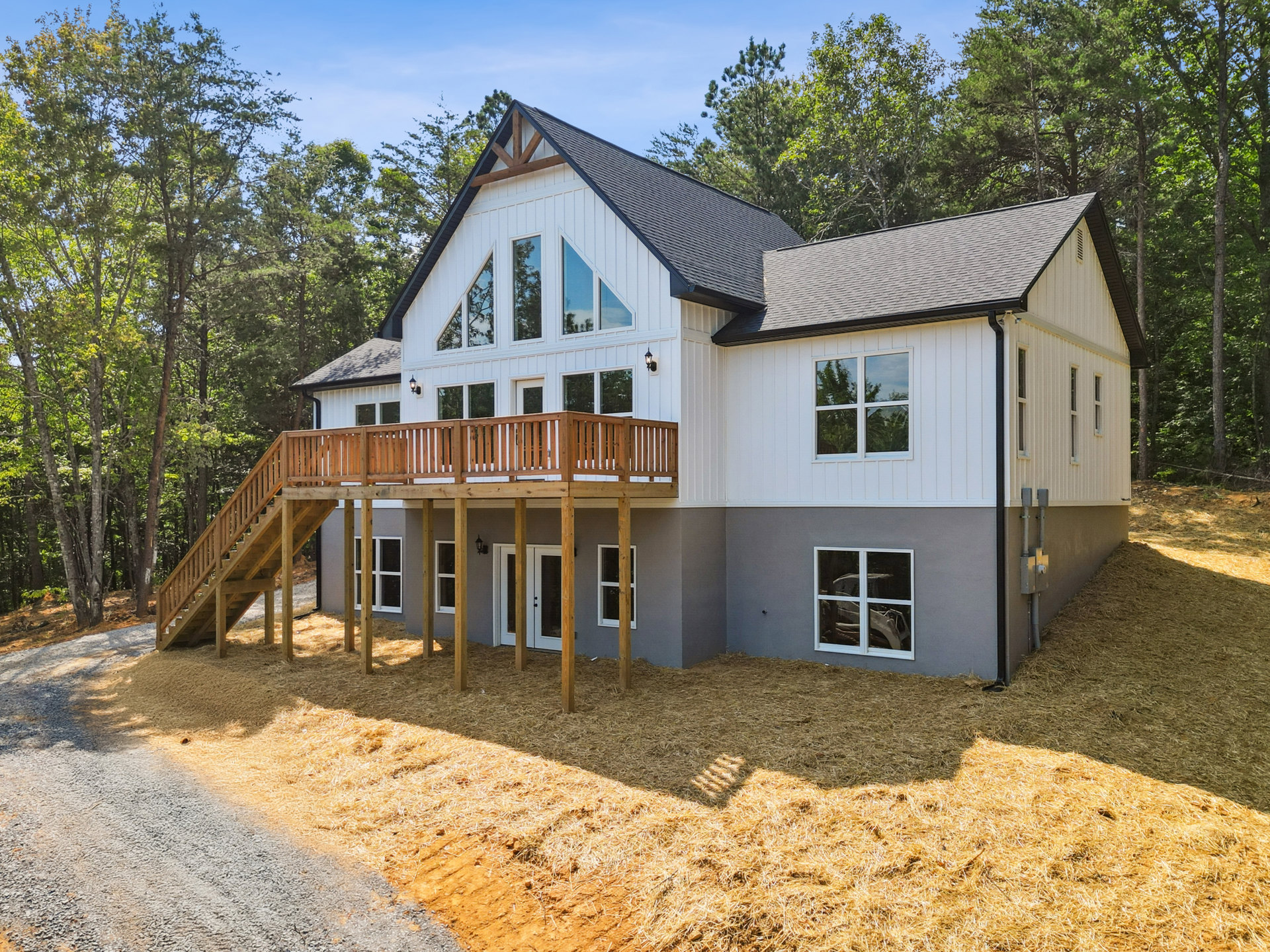 Two-story house with white-framed windows, wood siding, and a spacious wooden deck overlooking a landscaped yard with mature trees reflected in the glass
