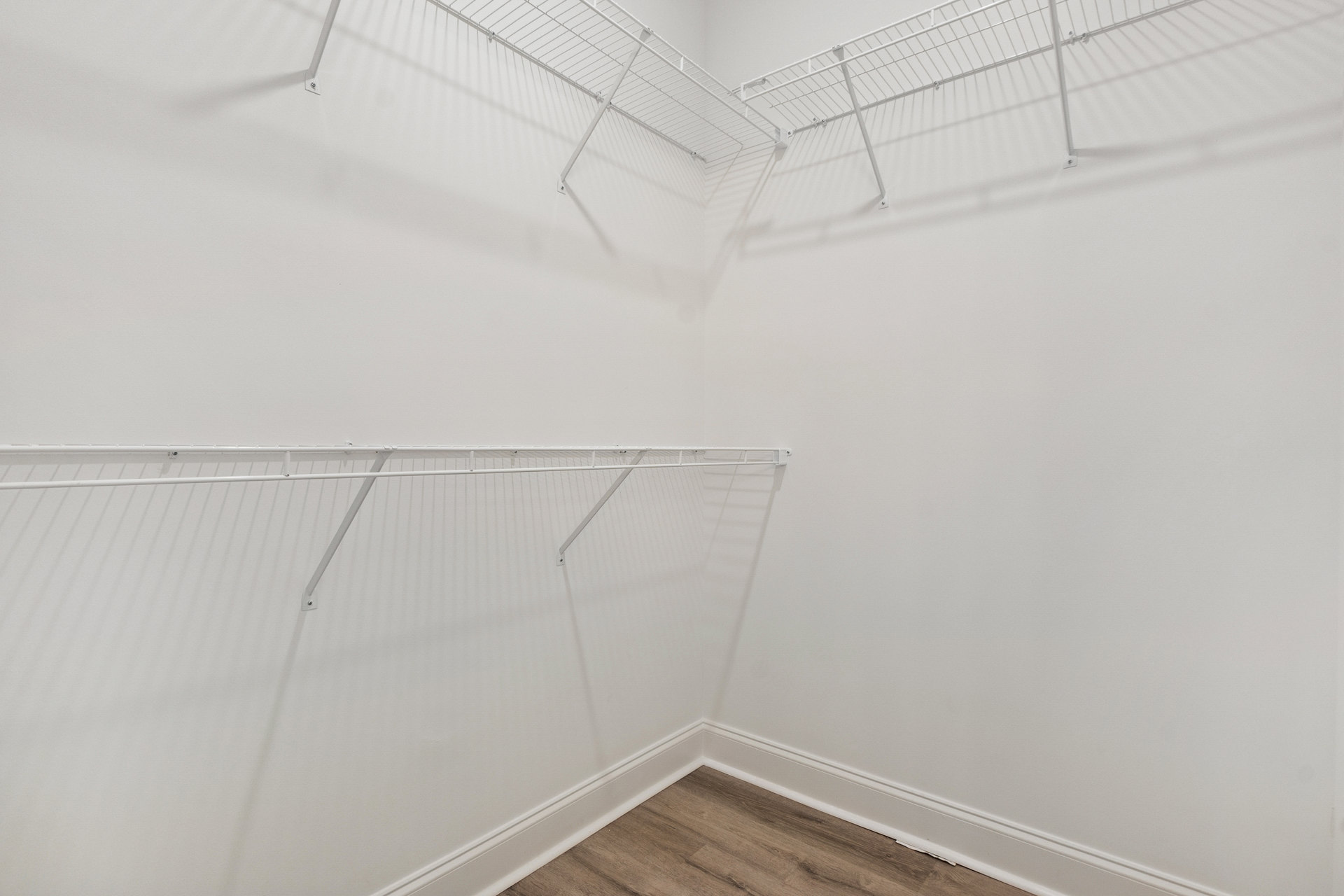 White built-in shelves along plaster wall, wood floor with white baseboard, clothes rack mounted beside shelving.
