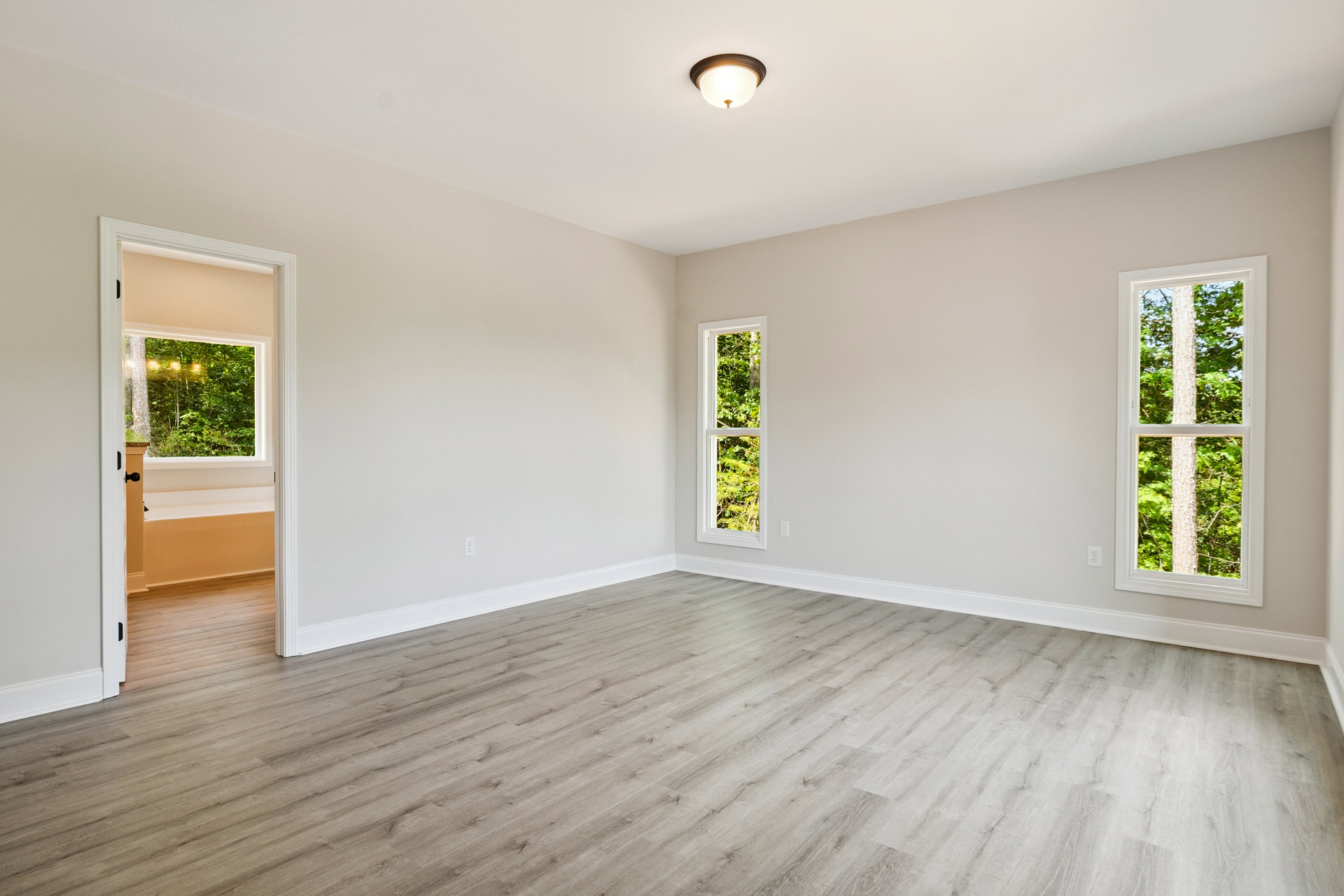Room with white plaster walls, hardwood floor, large window overlooking trees, modern pendant light fixture, and doorway visible.