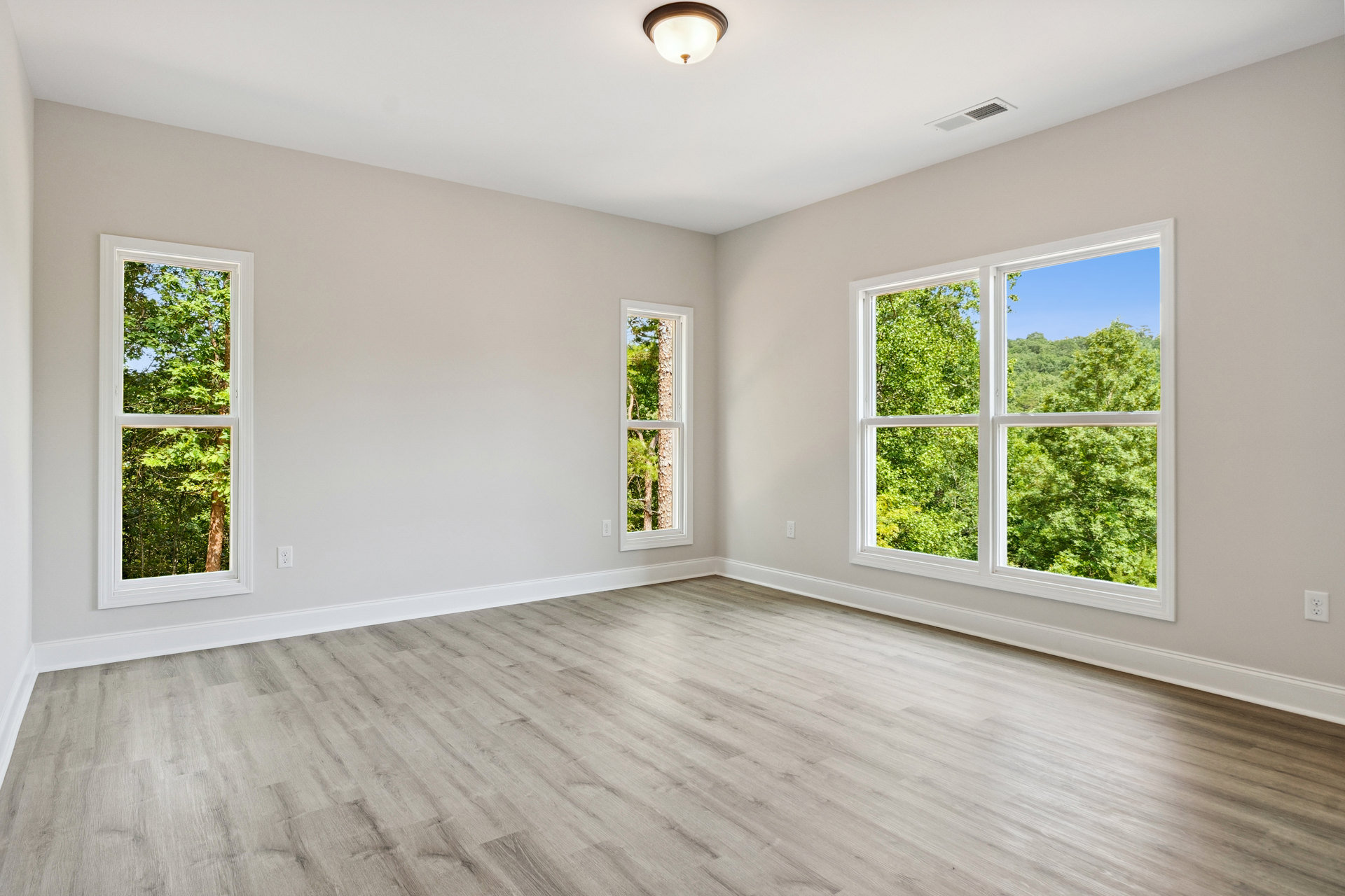 Spacious room featuring large windows with views of trees, wood flooring, and a ceiling-mounted light fixture