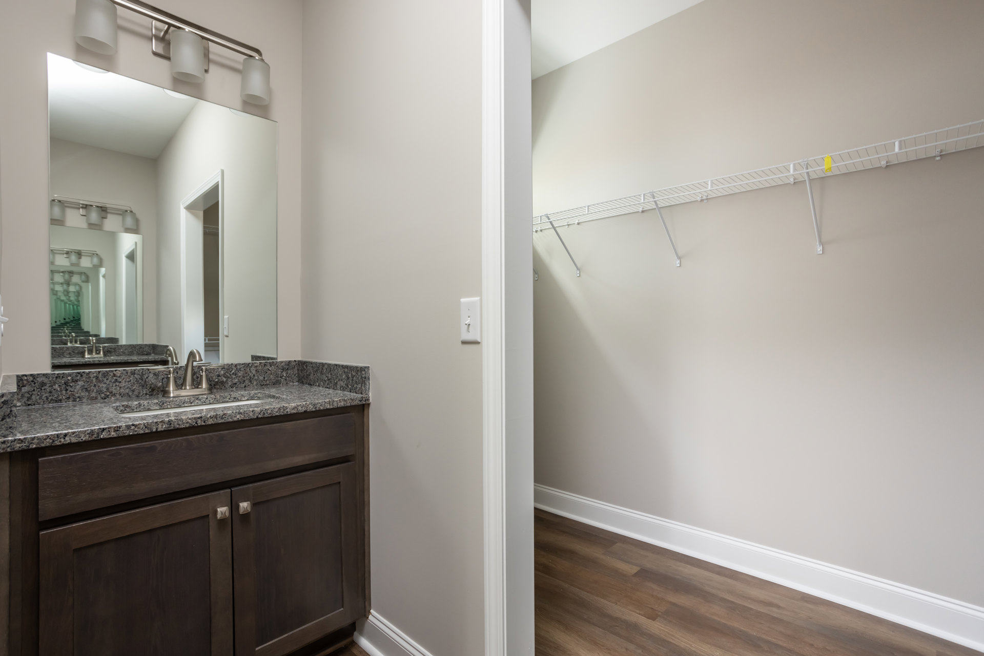 Modern bathroom with white tile walls, large mirror above a sleek countertop sink, chrome faucet, light wood cabinetry, and a white shelf mounted on the wall.