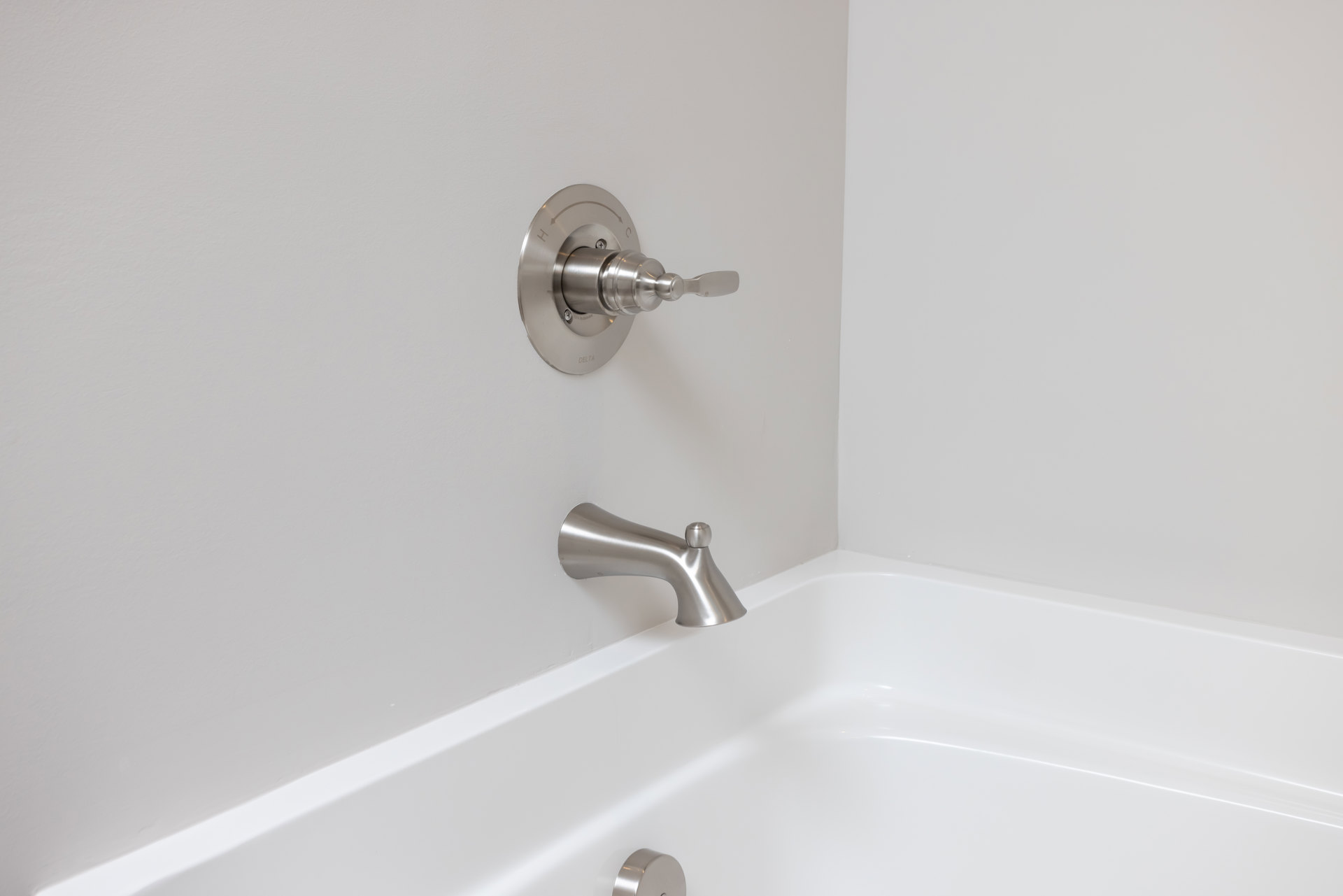 White bathtub with curved edge, silver faucet, and round chrome knob against light-colored bathroom wall