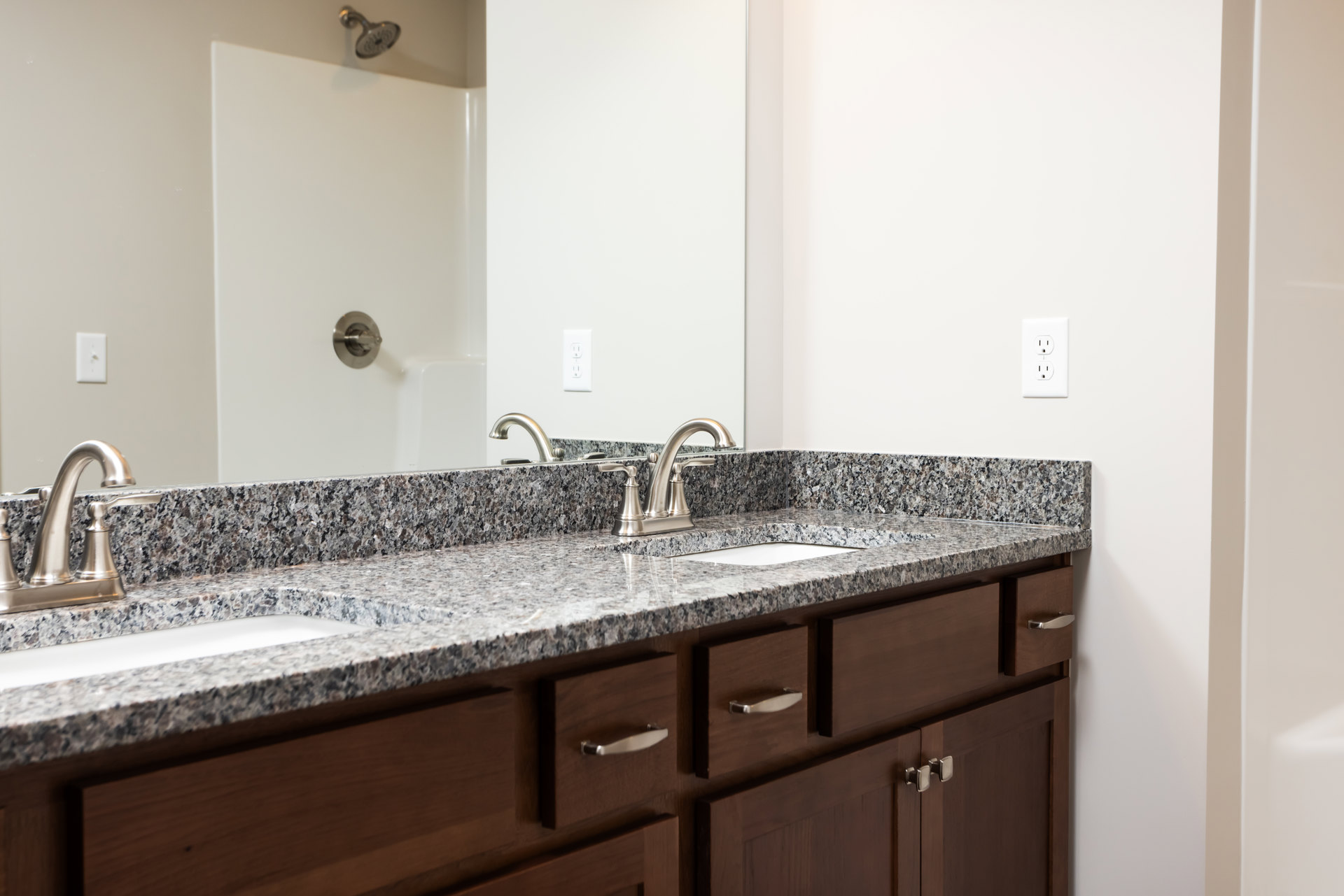 Granite countertop bathroom with undermount sink, chrome faucet, wall-mounted mirror, tile backsplash, and white cabinetry