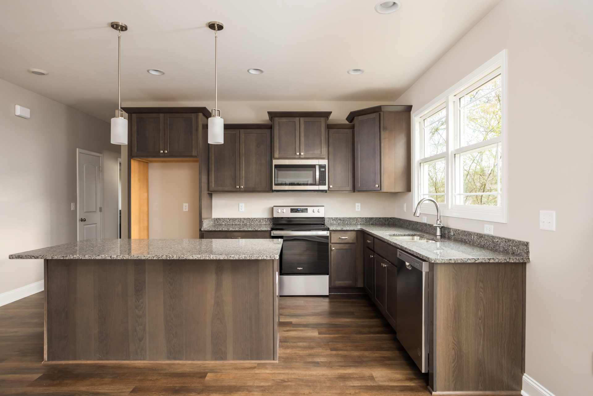 Granite countertops with wood paneling, black stove, built-in microwave, white bottle with black lid, stainless steel sink, and light cabinetry in a custom kitchen.