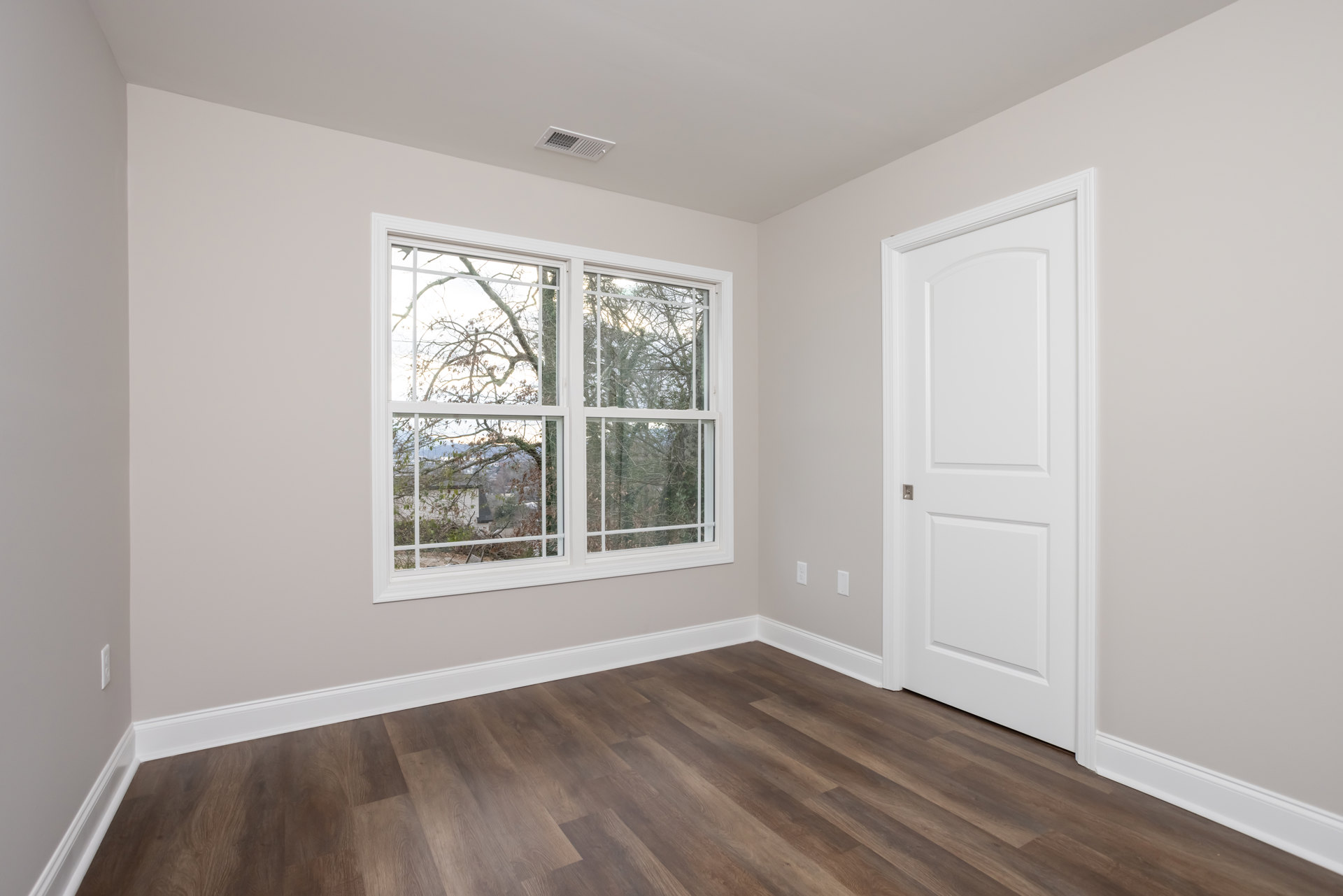 Wood floor with white baseboard, white square-framed door with silver handle, window showing tree branches outside