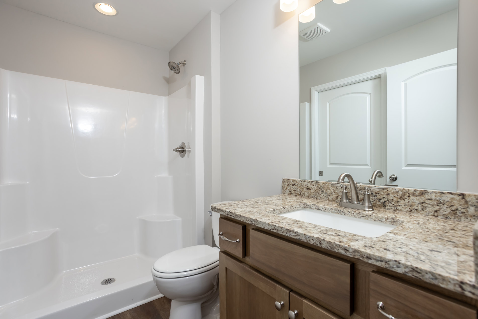 Modern bathroom with white tile shower, wall-mounted sink, closed toilet, salt and pepper shakers on stone countertop, chrome faucet, and showerhead with multiple holes