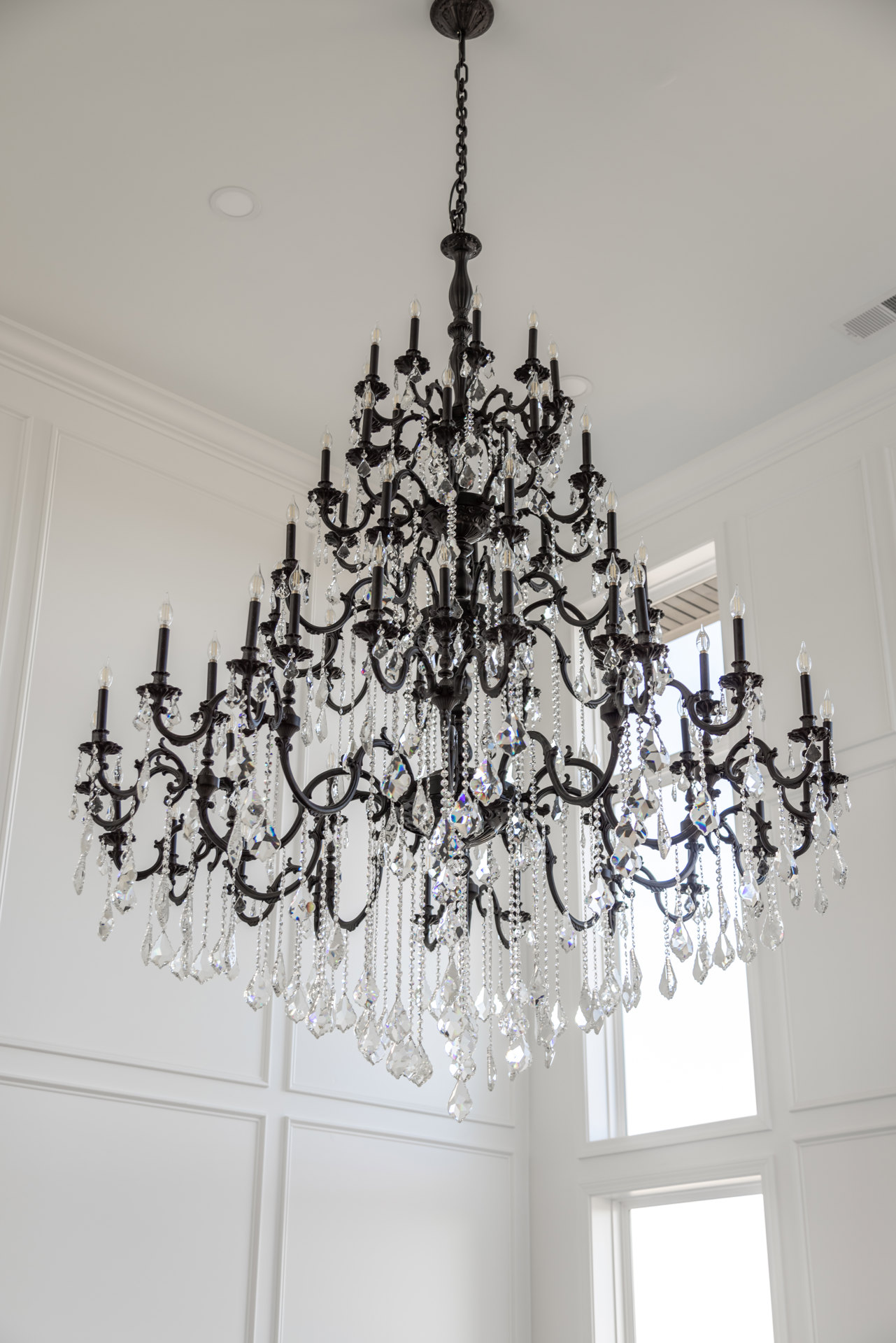 Crystal chandelier with hanging prisms suspended from white ceiling, adjacent to white door and window, illuminated interior space.