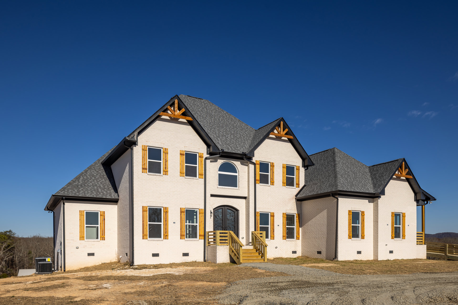 White farmhouse-style home with multiple windows, wooden exterior stairs, and a gabled roof under a clear blue sky
