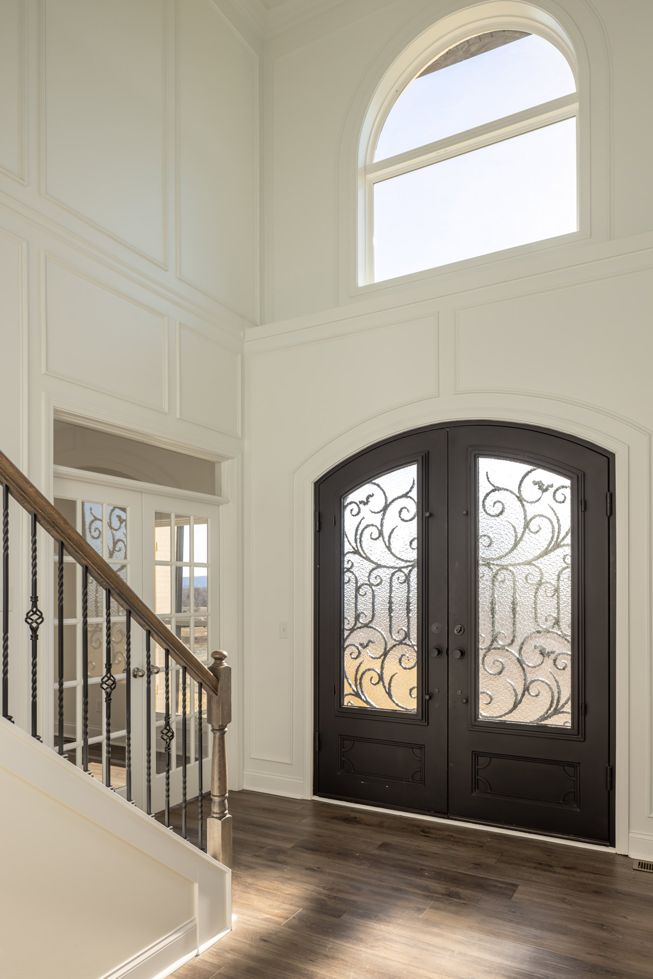 Double glass-paneled doors beside a staircase with wood railing, white-framed window, wood flooring, and black interior door