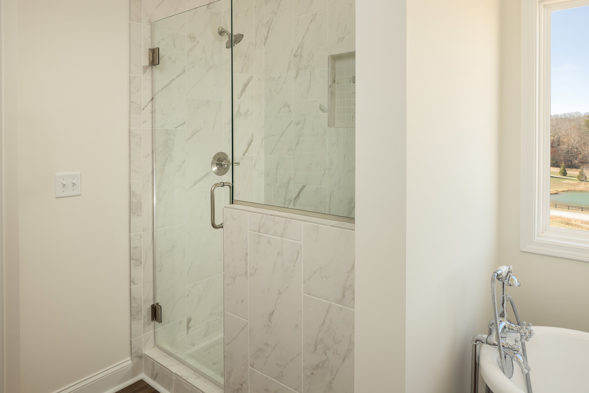 Frameless glass shower enclosure with chrome hardware, white tile walls, and a modern faucet in a contemporary bathroom
