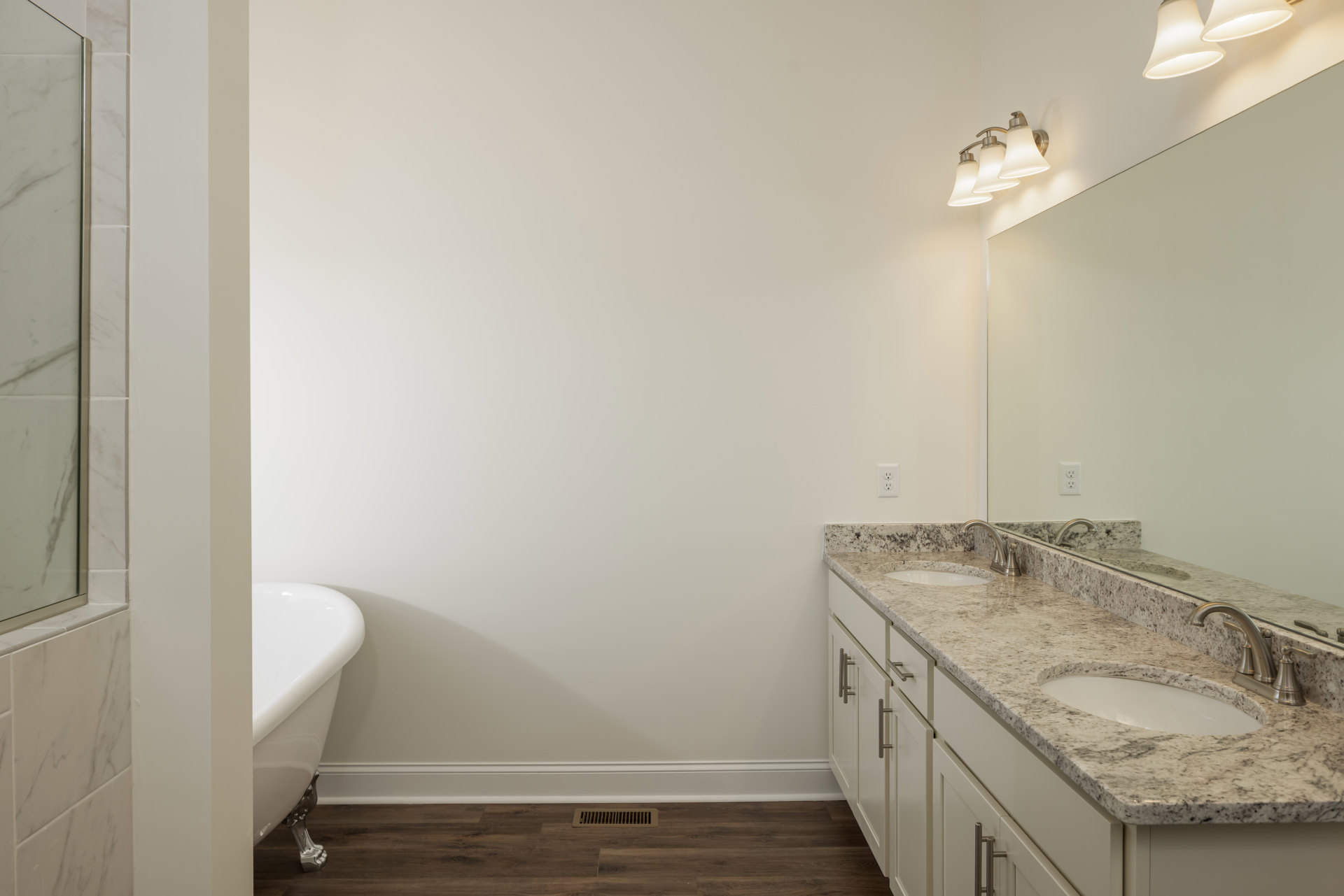 Bathroom featuring marble countertops, freestanding bathtub, undermount sink with chrome faucet, large wall mirror, glass shower door, white walls, and modern three-light fixture