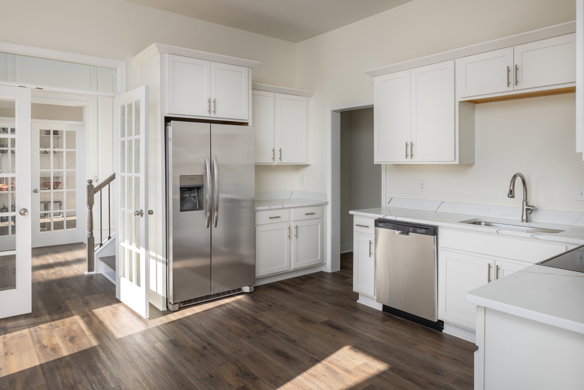White shaker cabinets, stainless steel refrigerator with water dispenser, silver dishwasher, light quartz countertops, undermount sink, white door with matching trim, neutral tile