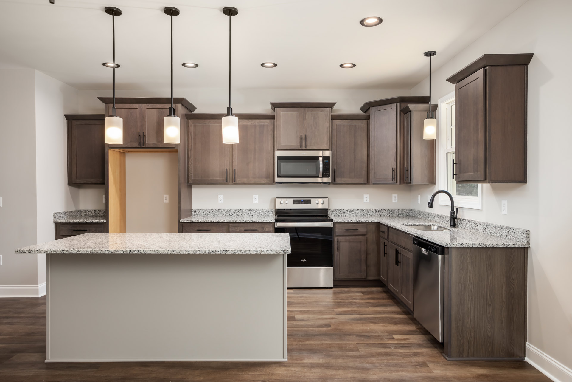Granite countertops and matching island in a kitchen with wood cabinetry, stainless steel appliances, tile backsplash, and pendant lighting