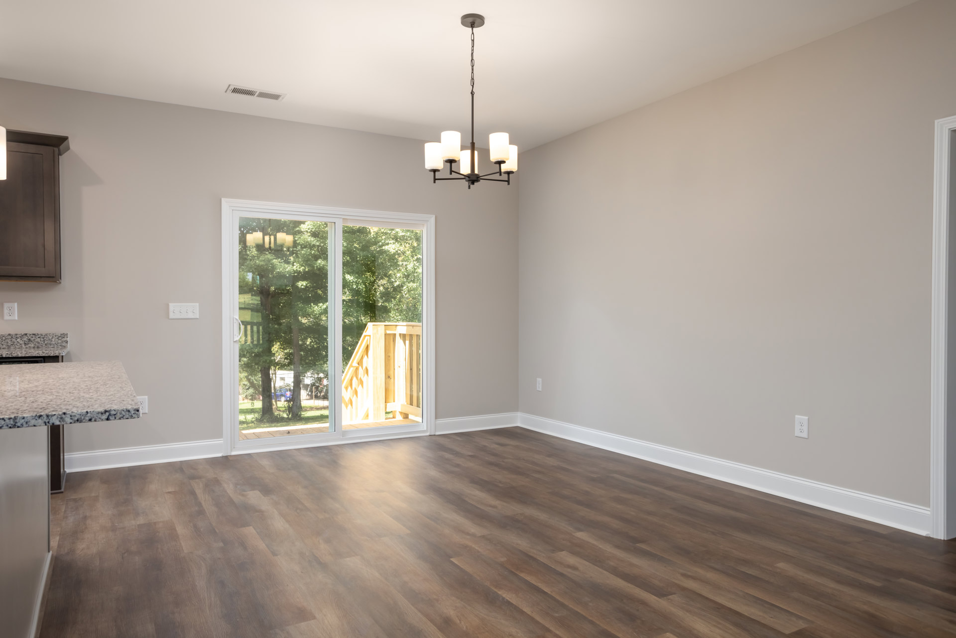 Hardwood floor room featuring an open white door, sliding glass door leading to a wooden railing outside, black speckled countertop, wall-mounted light fixture, and plaster walls.
