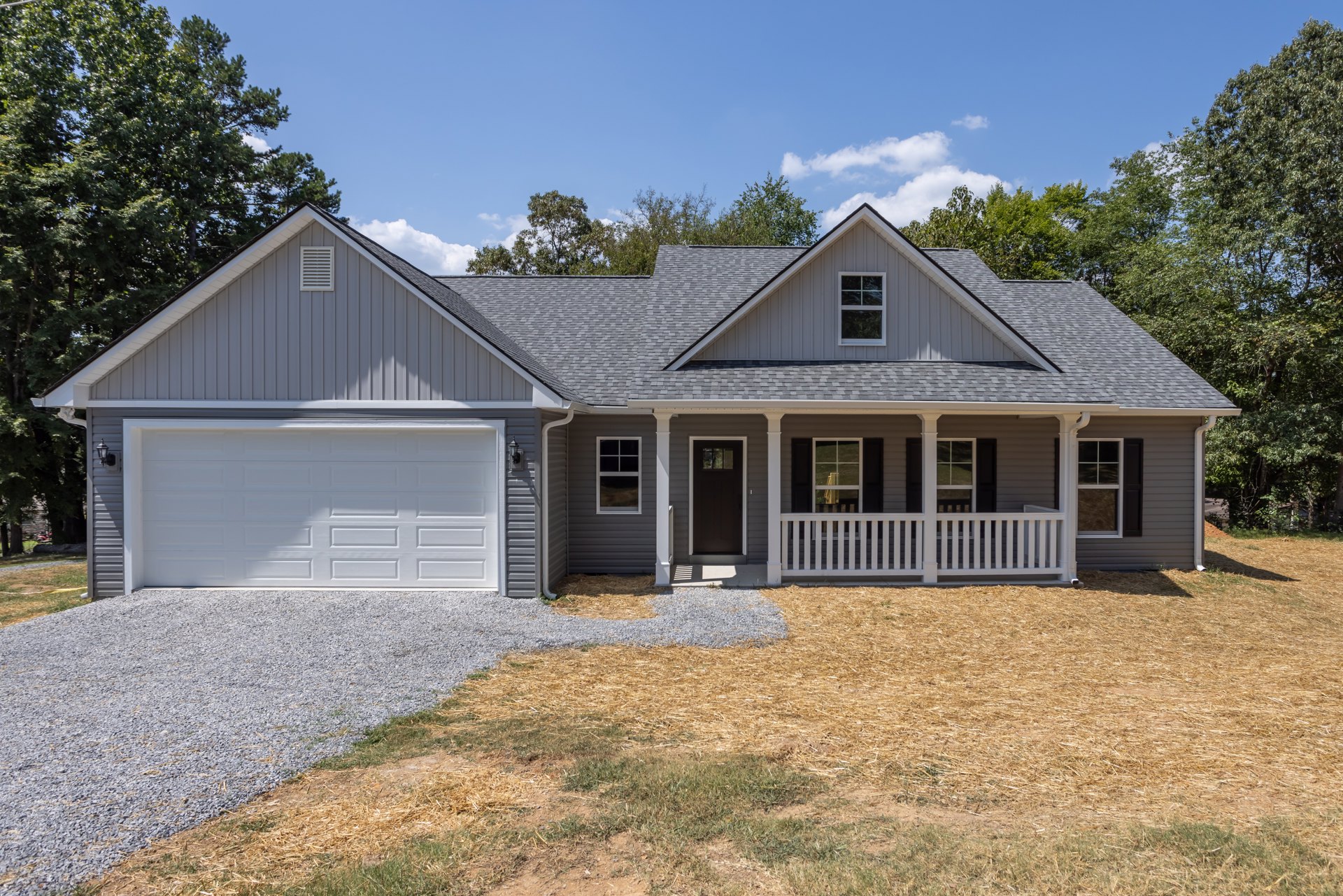 Two-story house with white-framed windows, attached garage featuring a windowed white door, covered porch with white railing, concrete driveway, and landscaped front yard with