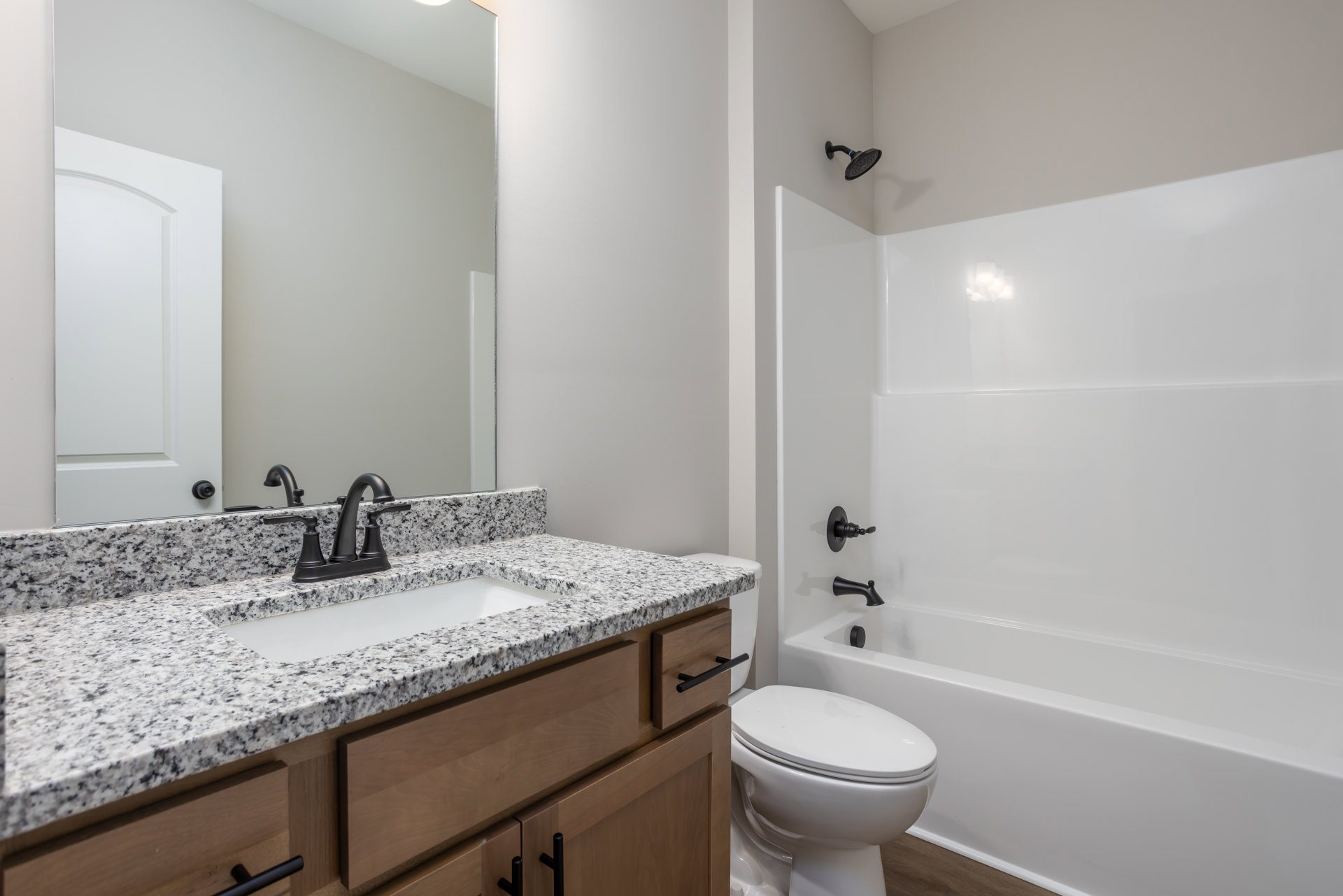 Modern bathroom featuring a white sink with chrome faucet, frameless mirror above a light-colored countertop, glass-enclosed shower with tiled walls, and a white toilet adjacent to