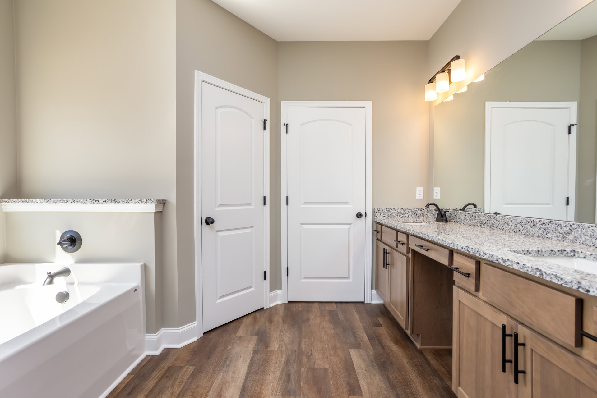 Bathroom with freestanding white bathtub, chrome faucet, double white doors with black hardware, tile flooring, wall-mounted light fixture, and visible light switch