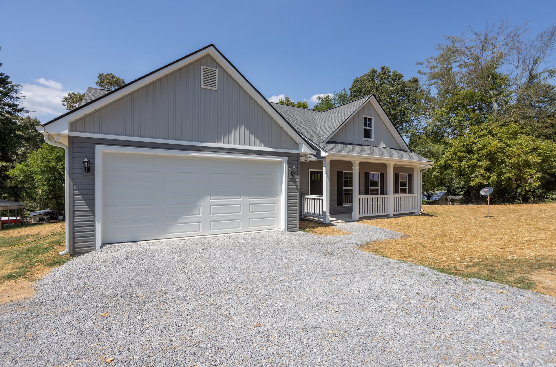 White garage door beneath black roof, concrete driveway, light-colored siding, wall vent, small tree and shrubs along front yard