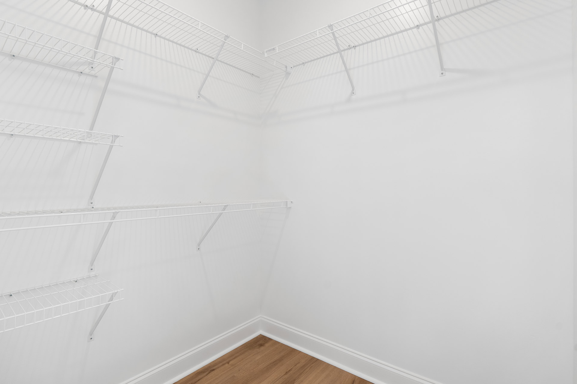 White built-in shelves in a corner room with wood flooring and white trim, plaster walls, and a smooth ceiling.