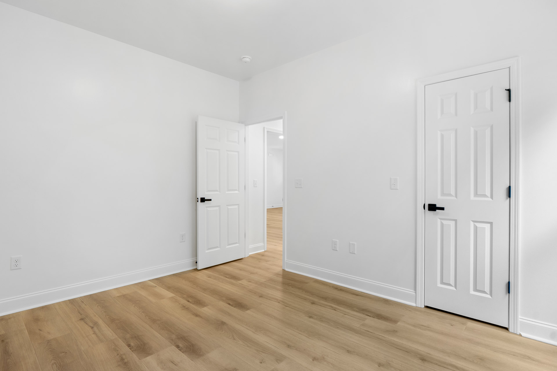 White walls and doors, wood flooring with white trim, black door handle