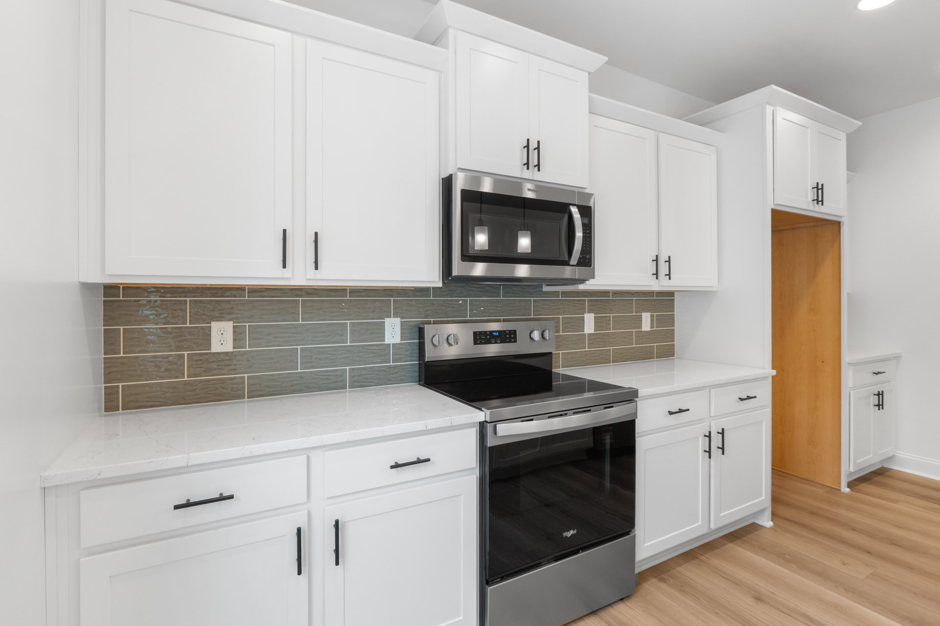 White kitchen cabinets with black appliances, built-in microwave above stove, light countertops, and drawers.