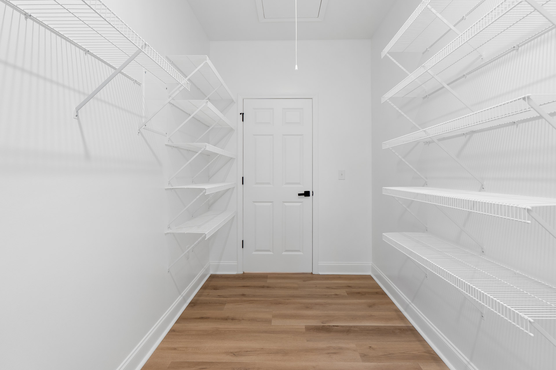 White room with wood flooring, built-in white shelves on plaster walls, and a white door with a black handle.