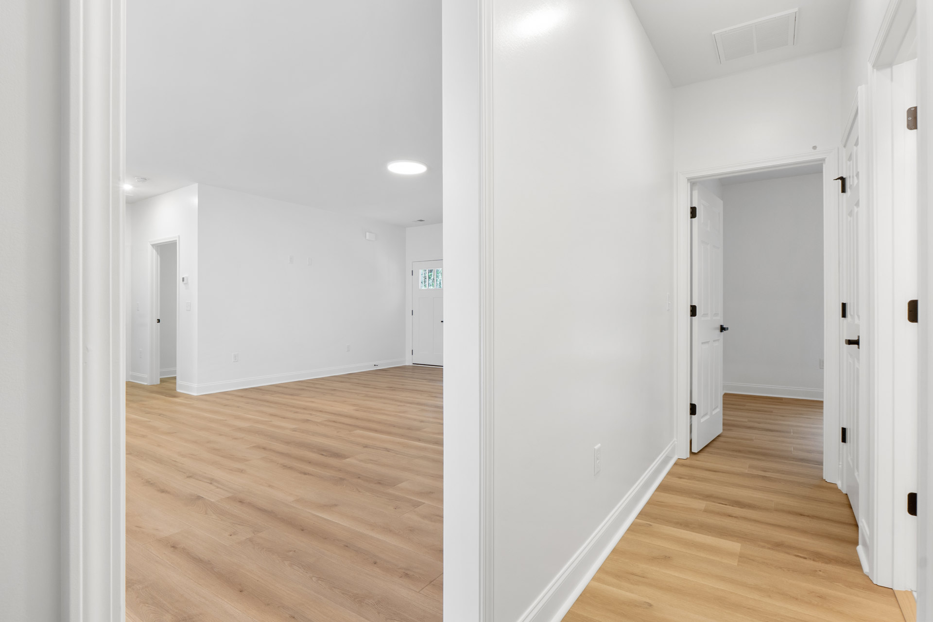 Hardwood floor room with white walls, white door and frame, ceiling vent, and plaster ceiling