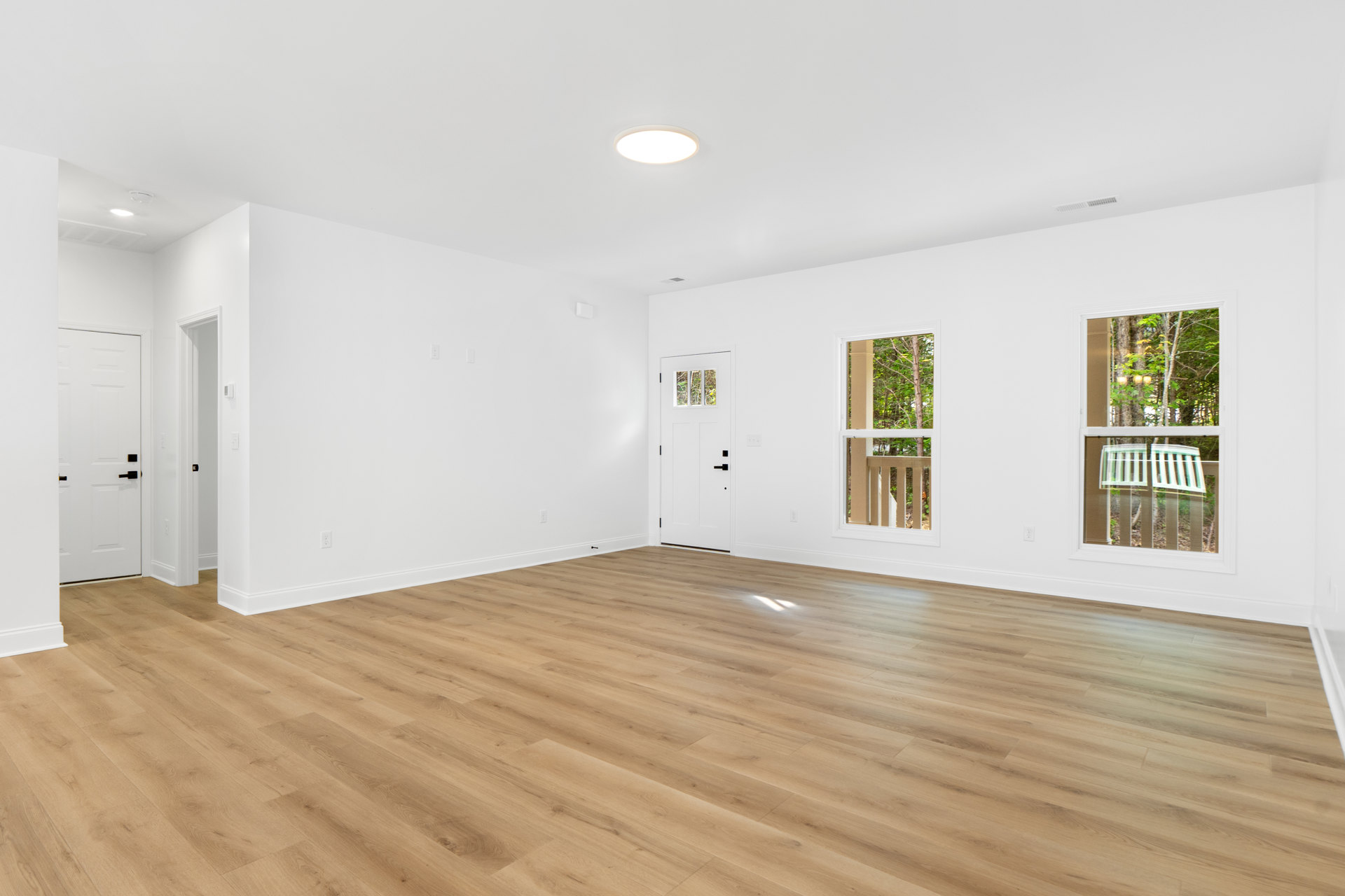 White walls and hardwood floor in a bright room with windows, white door featuring black handles, and a white bench along a fence.